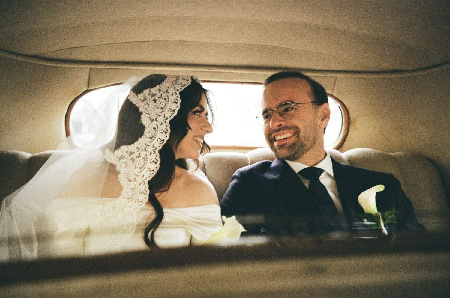 Newlyweds laughing in the back of a vintage car, on 35mm film