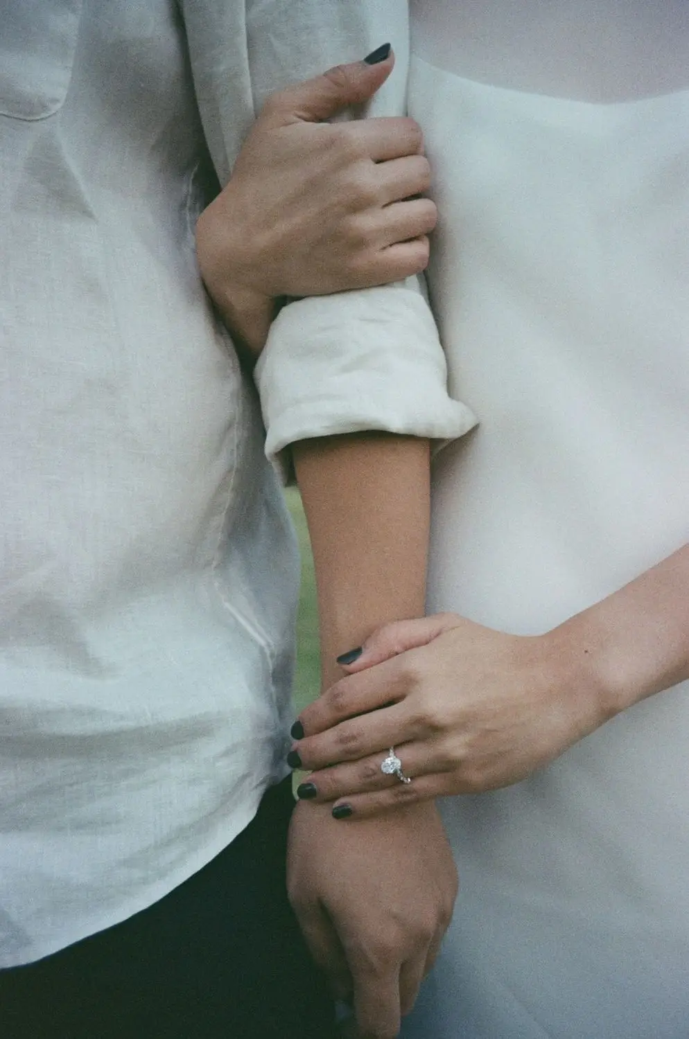 Close-up of hands with an engagement ring on a white dress, on 35mm film