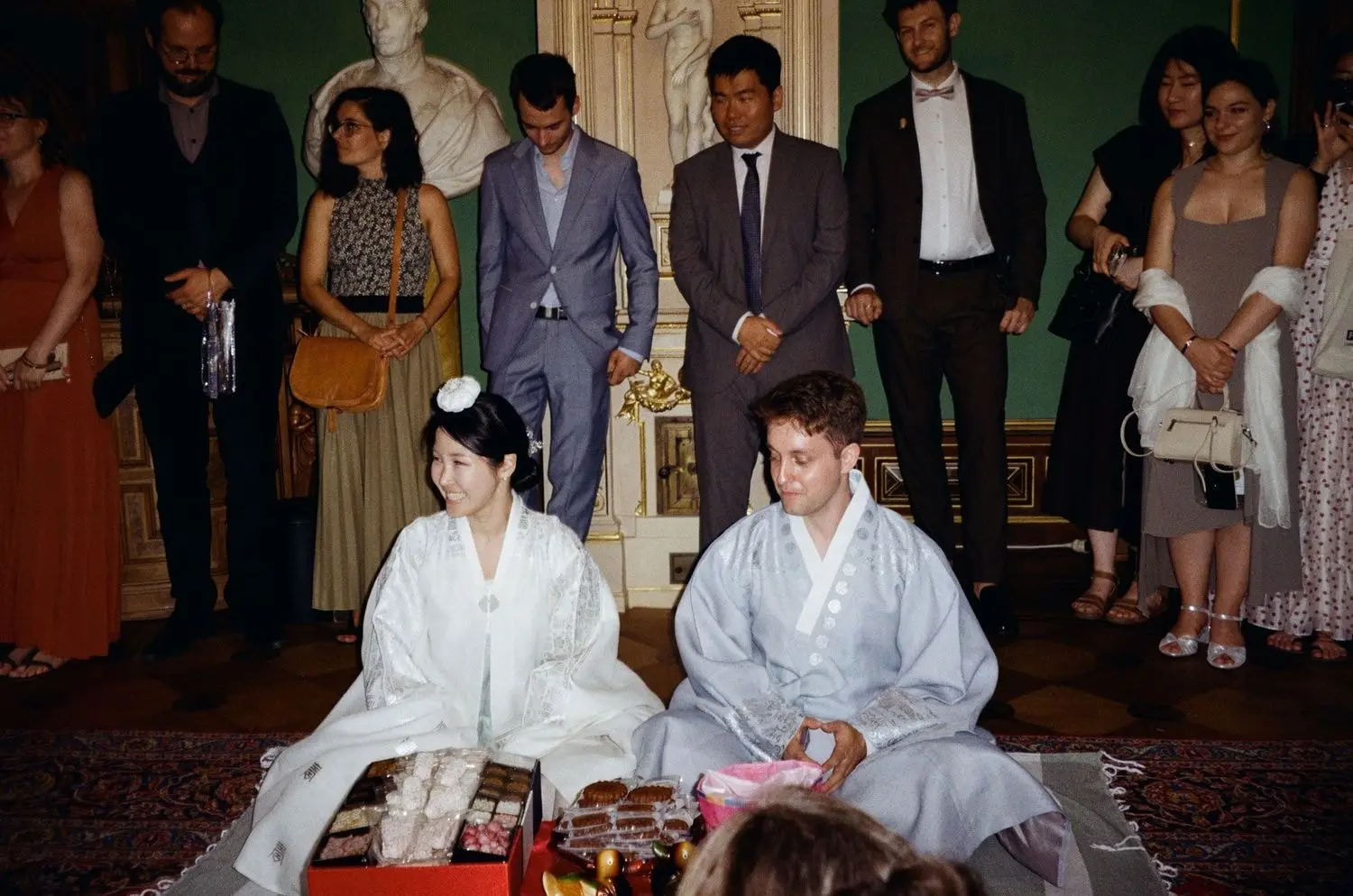 Couple in hanbok kneeling during the paebaek ceremony with guests, on 35mm film
