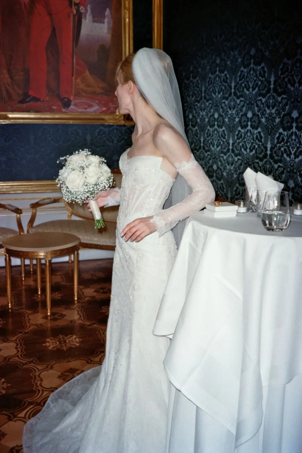 Bride in a lace gown by a painting in a palace room, on 35mm film