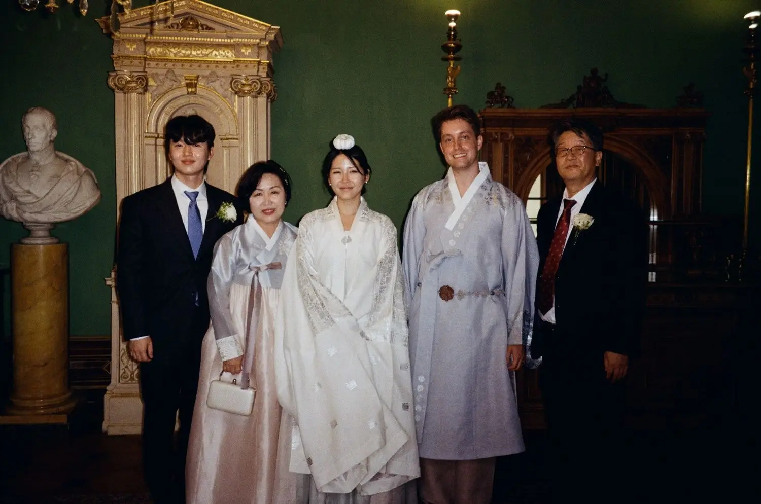 Couple in hanbok with their families in a palace room, on 35mm film
