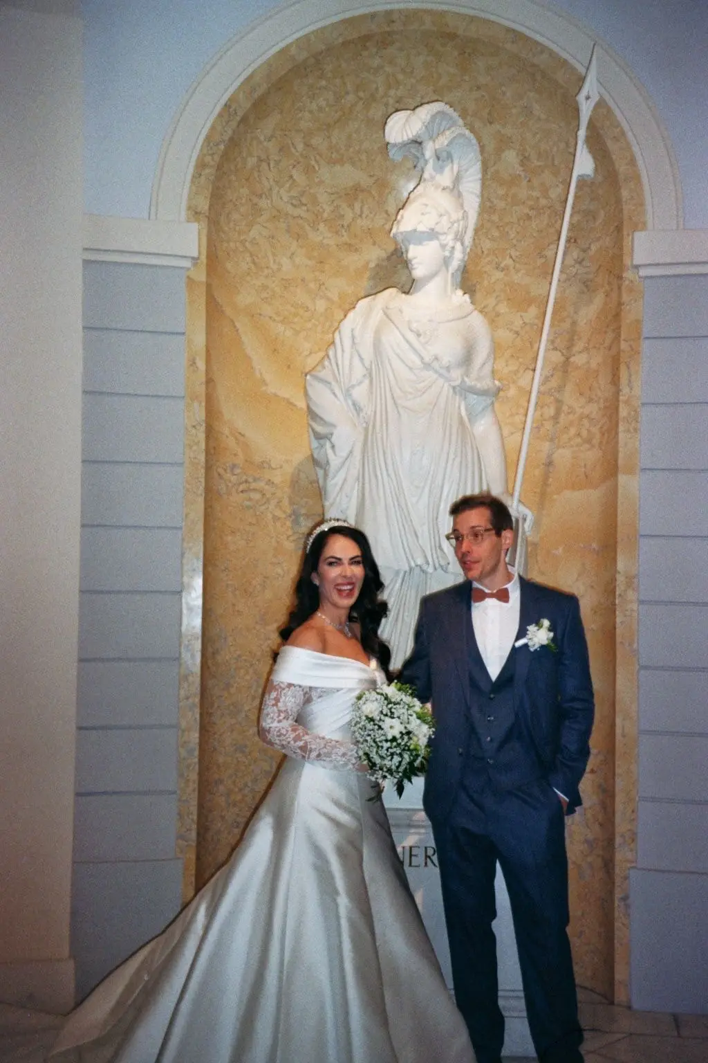 Bride and groom in front of a marble statue in a niche, on 35mm film