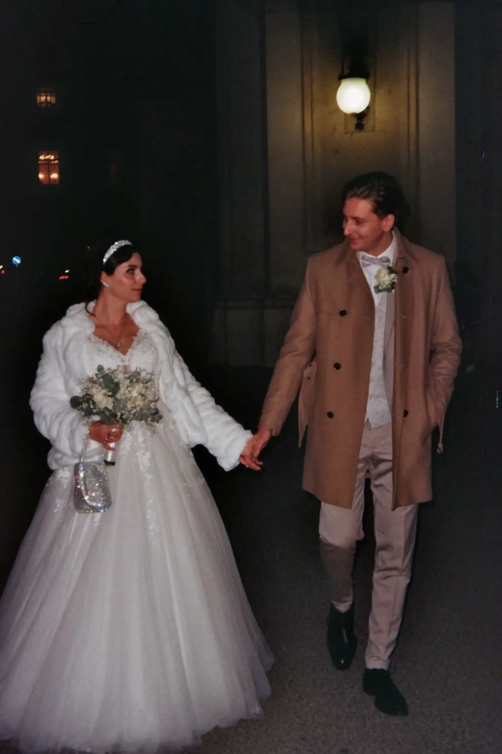 Bride in a white coat and groom walking at night, on 35mm film