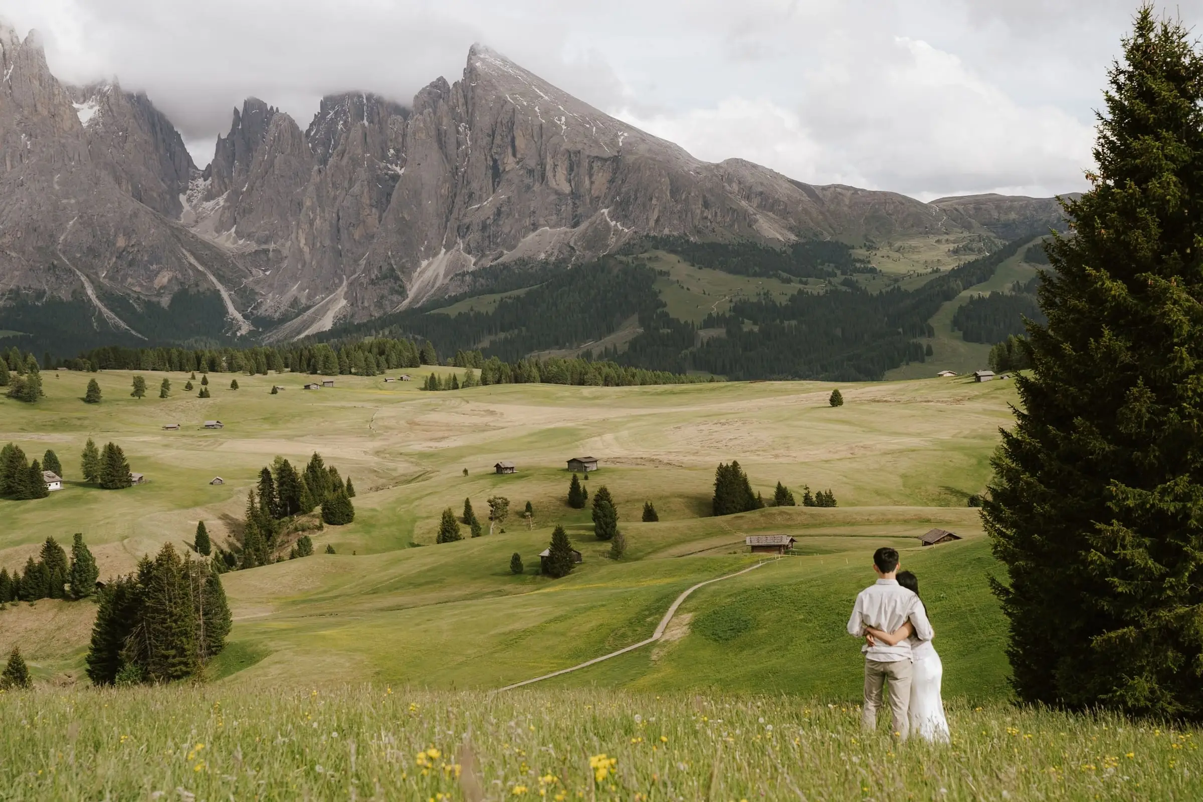Couple embracing in the meadow after the proposal, Sassolungo and Sassopiatto in the distance