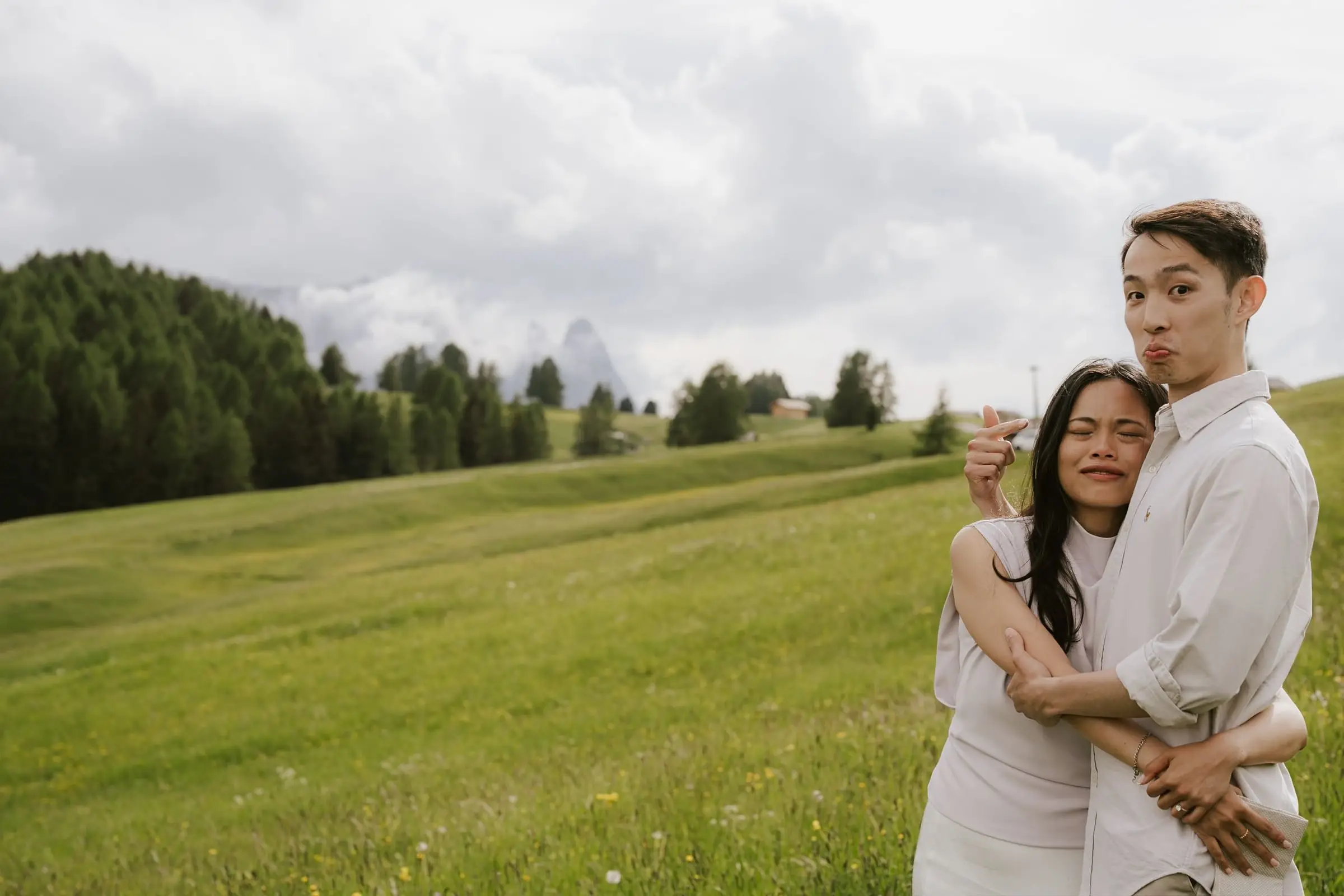 Couple hugging and pulling faces in a green alpine meadow
