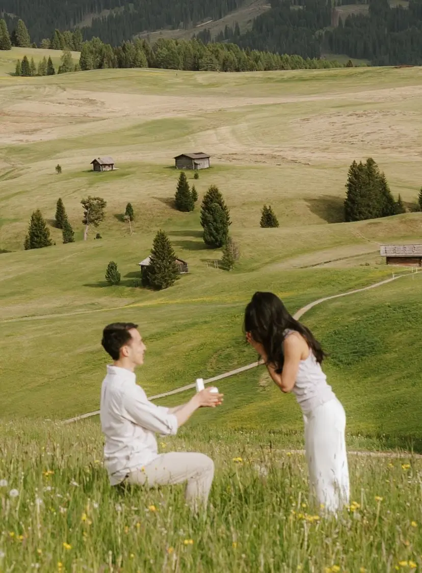 Surprised woman covers her face as her partner kneels with the ring on the Alpe di Siusi