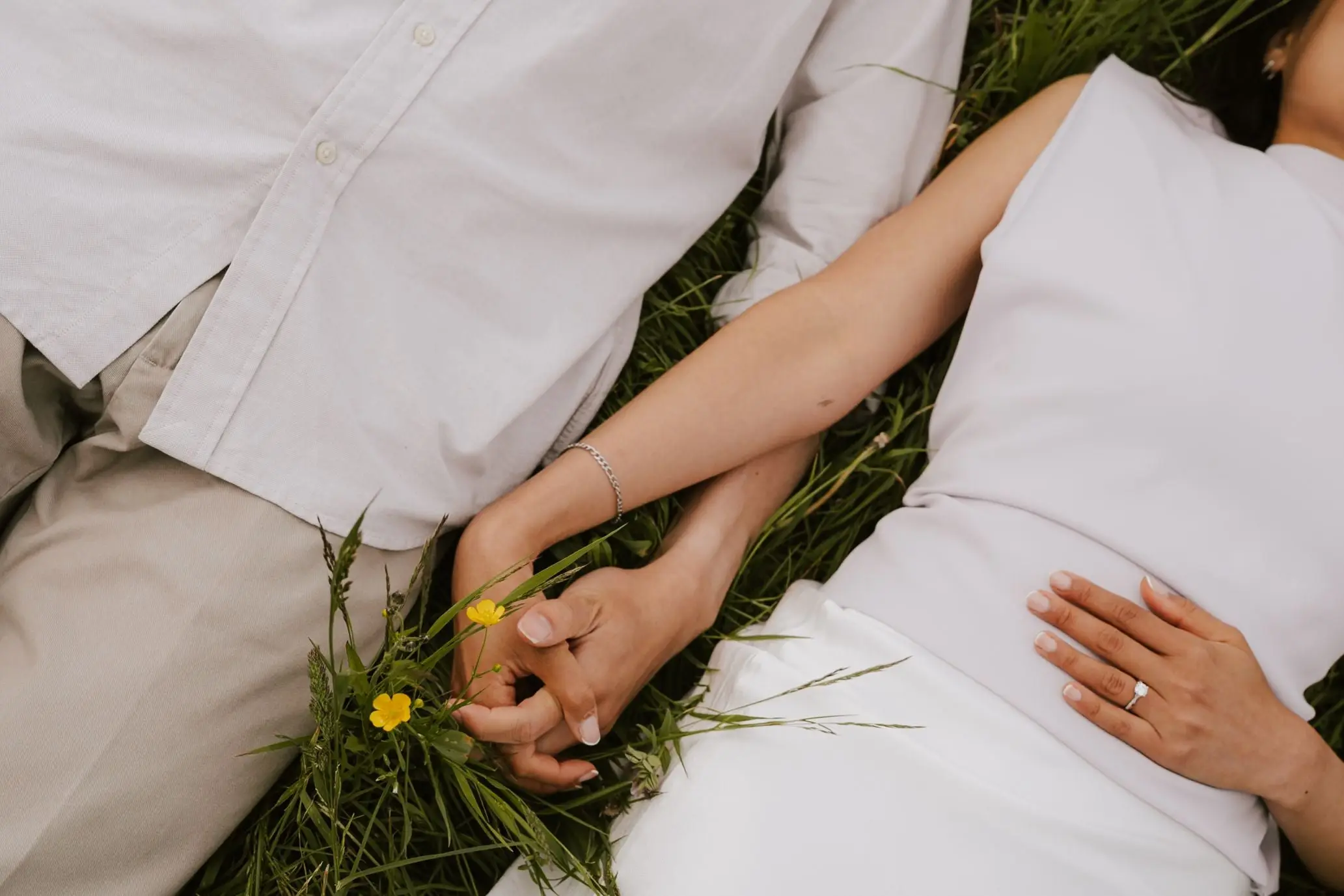 Close-up of the couple's hands and engagement ring, lying in the grass among wildflowers