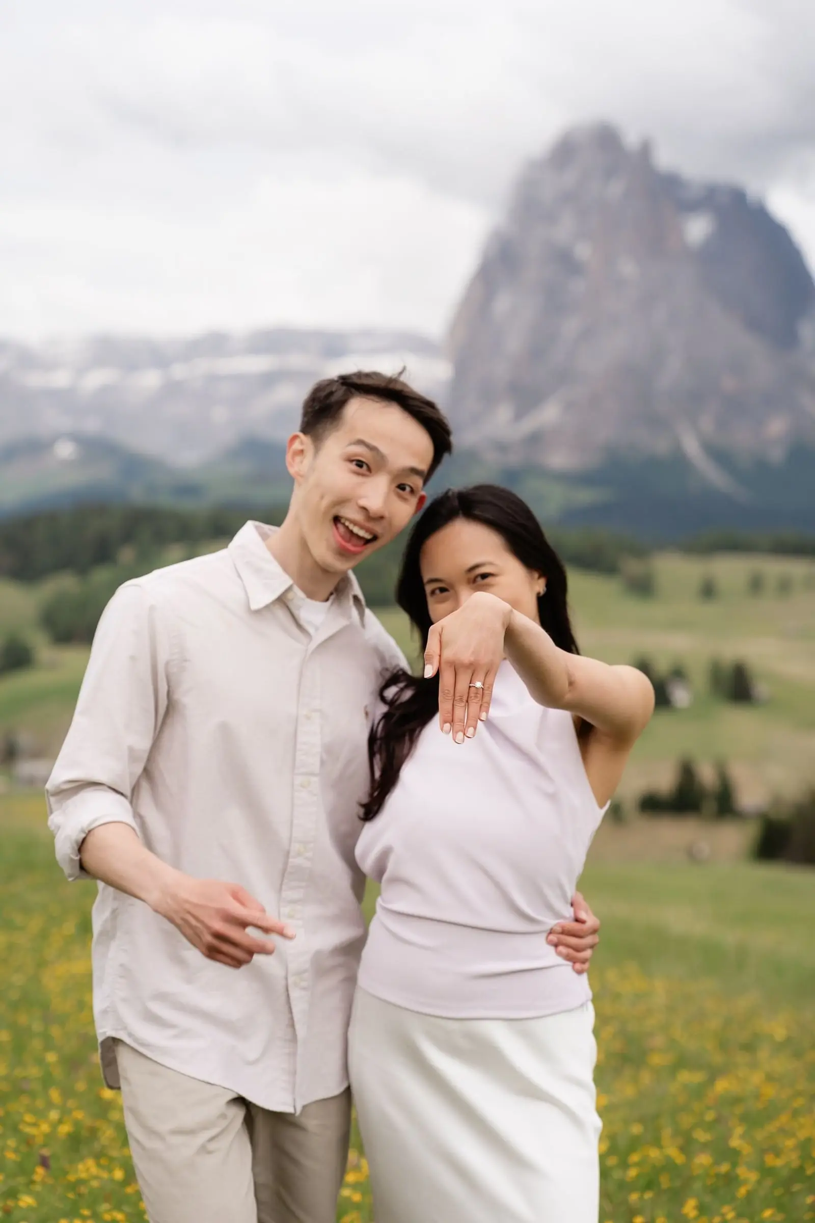 Newly engaged couple smiling, she holds up her ring with the Sassolungo behind them