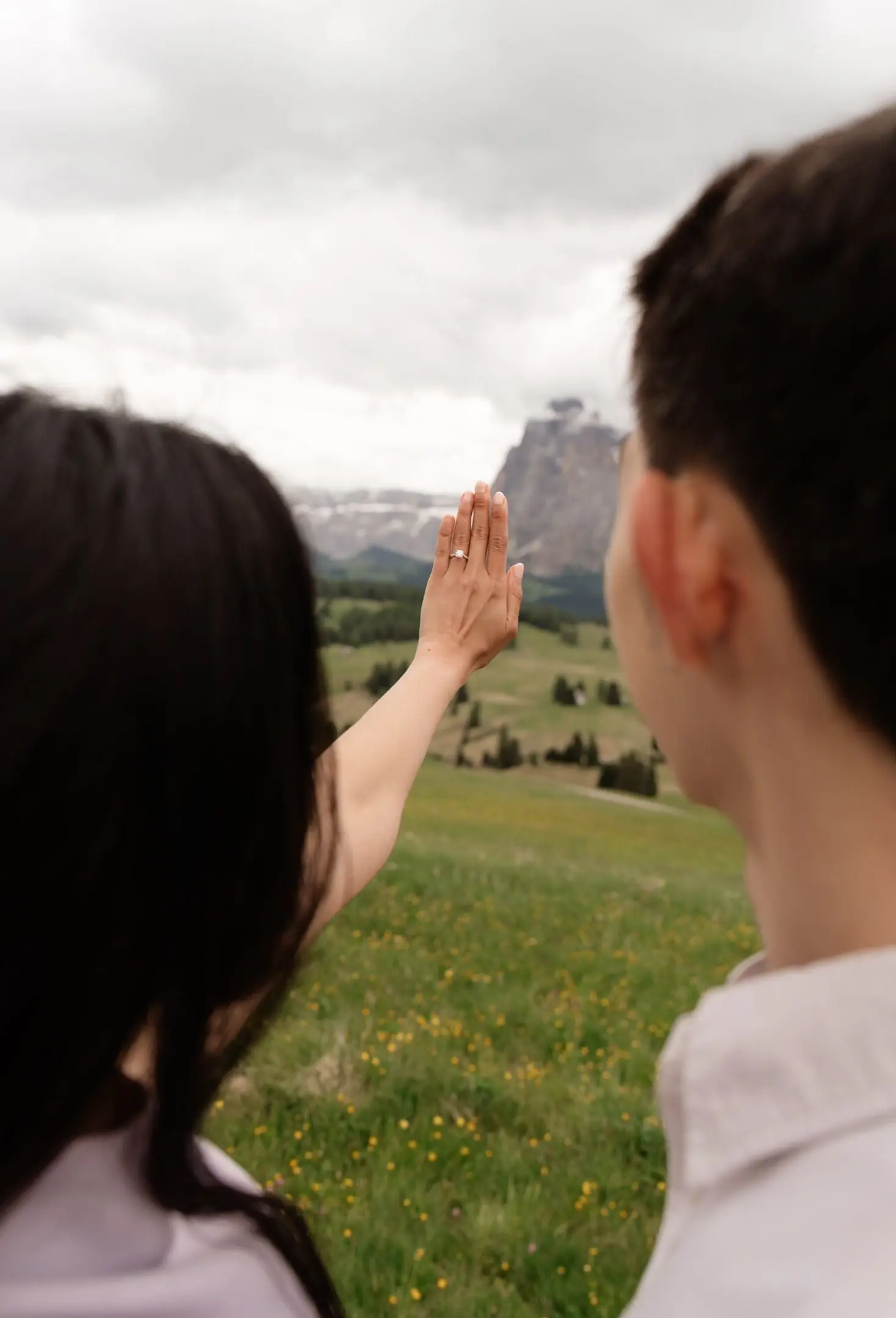 She raises her hand to show the ring against the mountains, seen over his shoulder