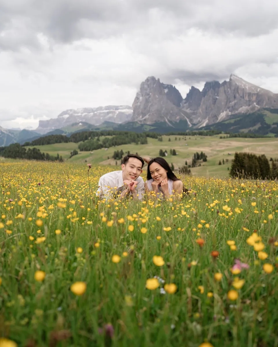 Couple sitting in a meadow of buttercups, mountains in the background