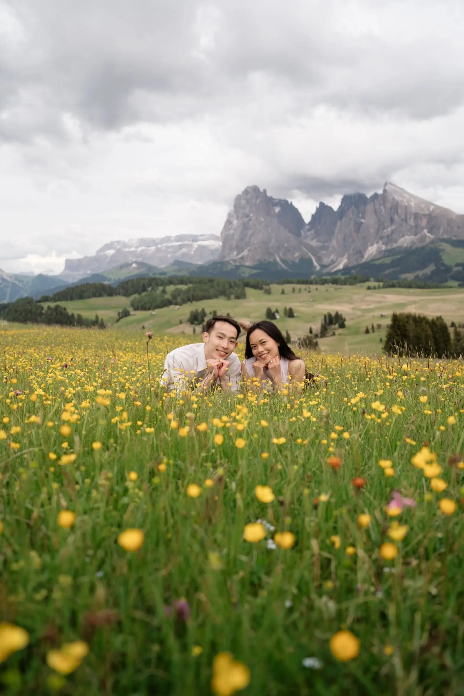 Couple sitting in a meadow of buttercups, mountains in the background