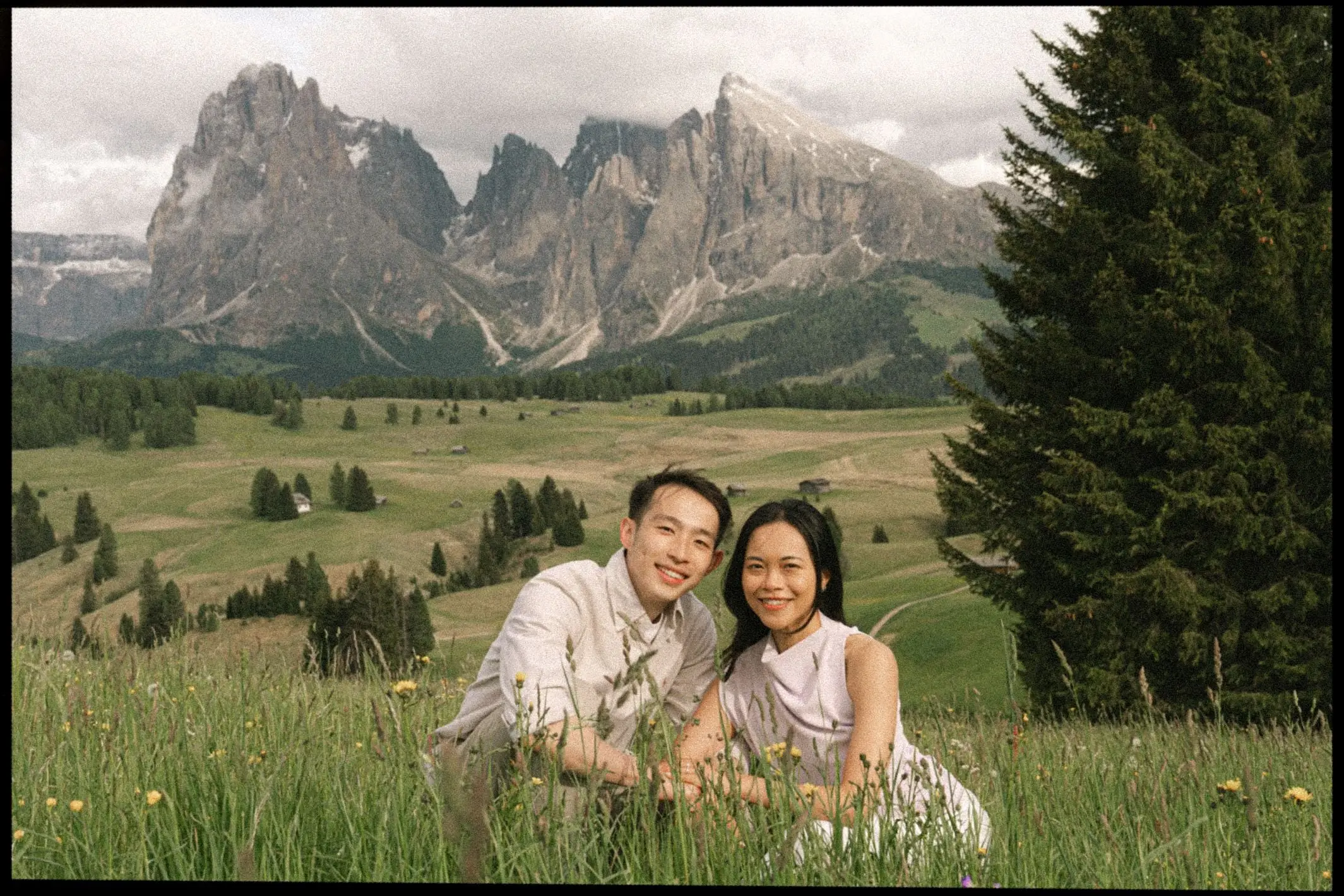 Couple smiling in the grass in front of the Sassolungo, framed with film borders