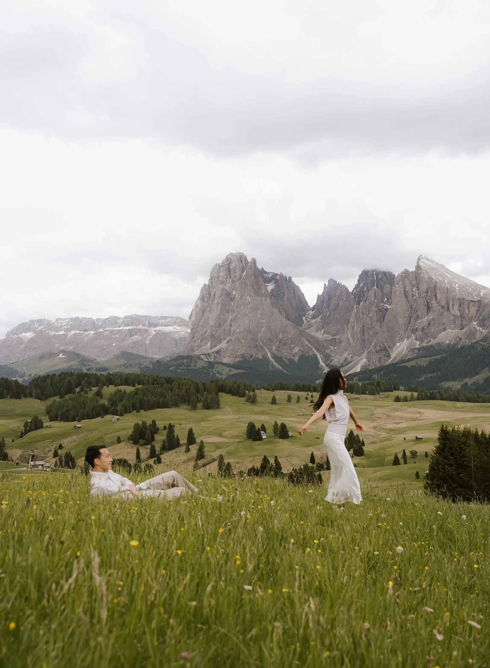 She twirls in the meadow while he lies in the grass, Dolomites behind them