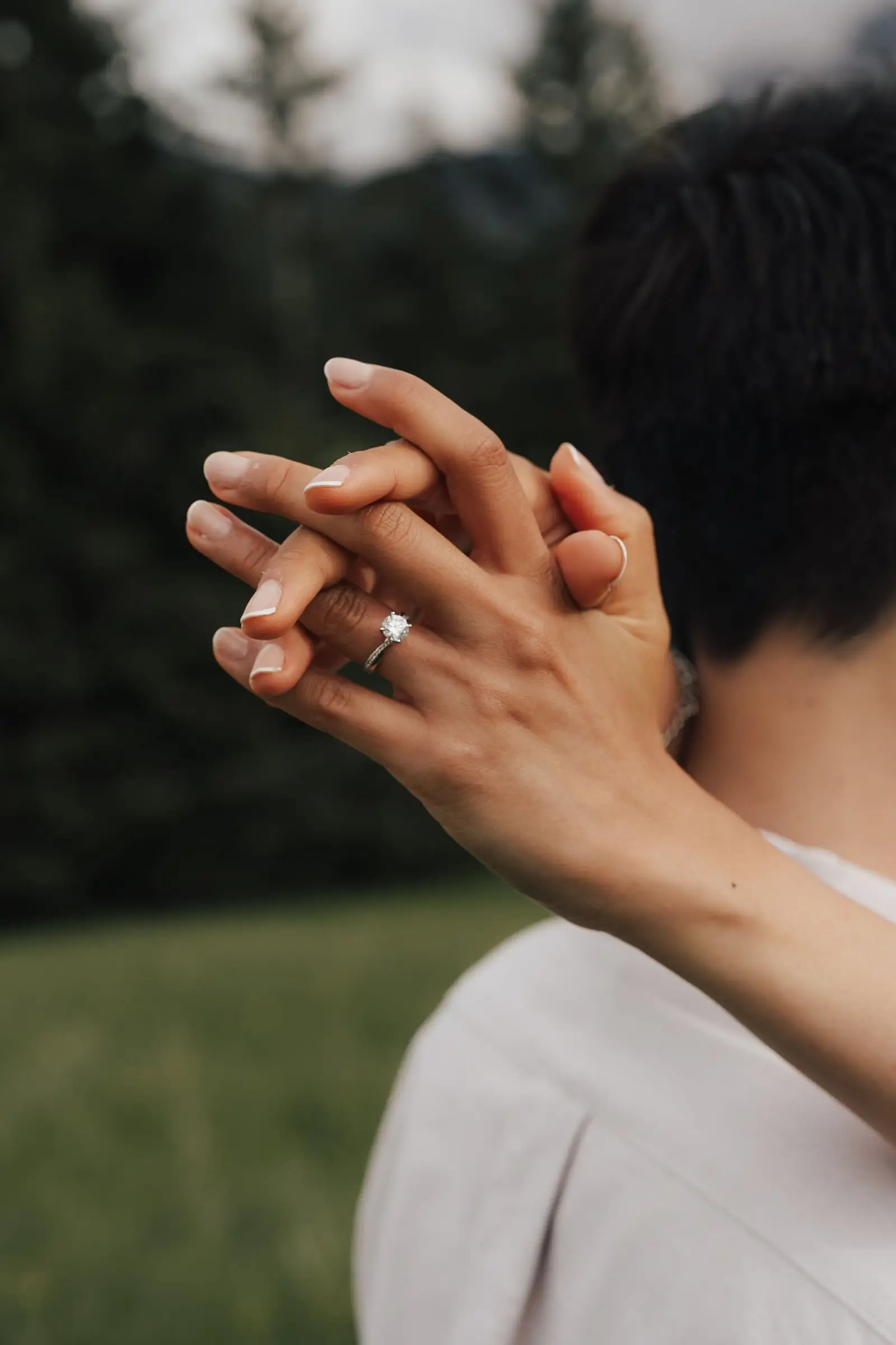 Close-up of her hand with the engagement ring resting on his shoulder
