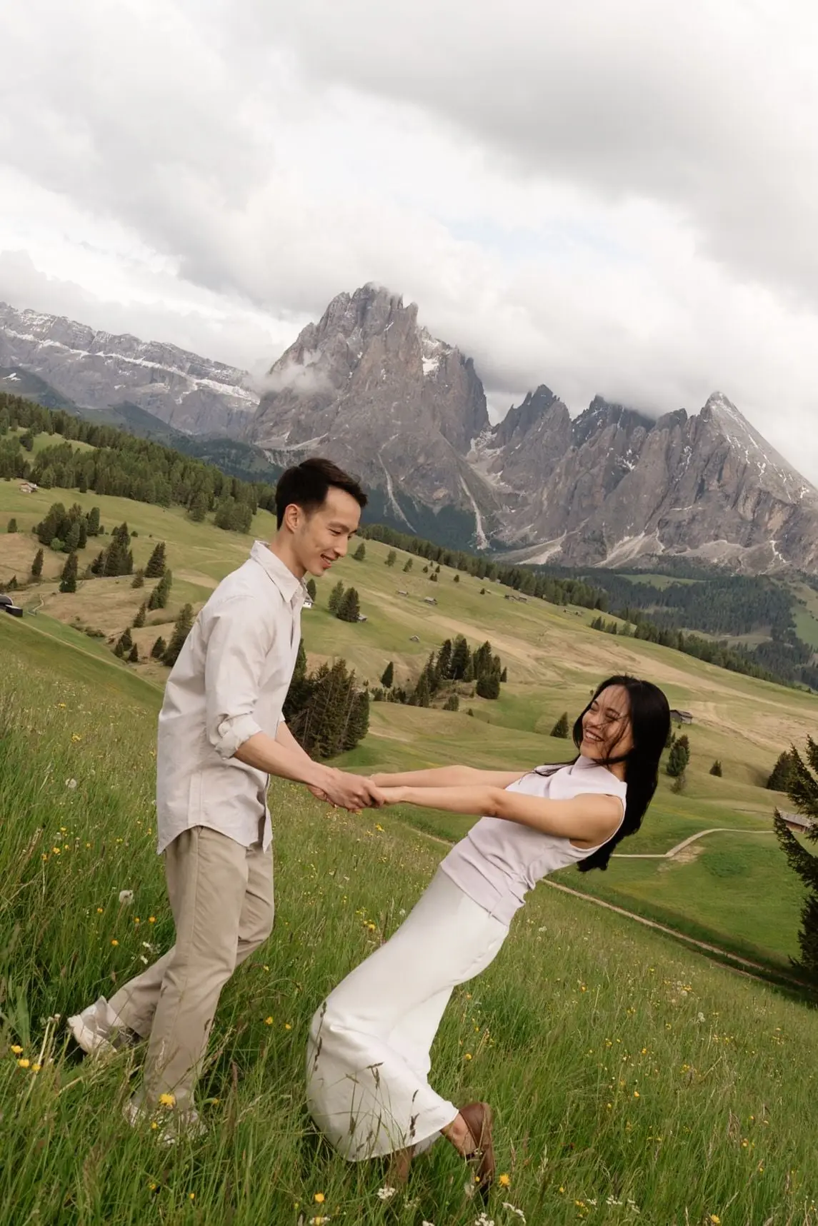 Couple swinging each other round on a grassy slope below the Sassolungo
