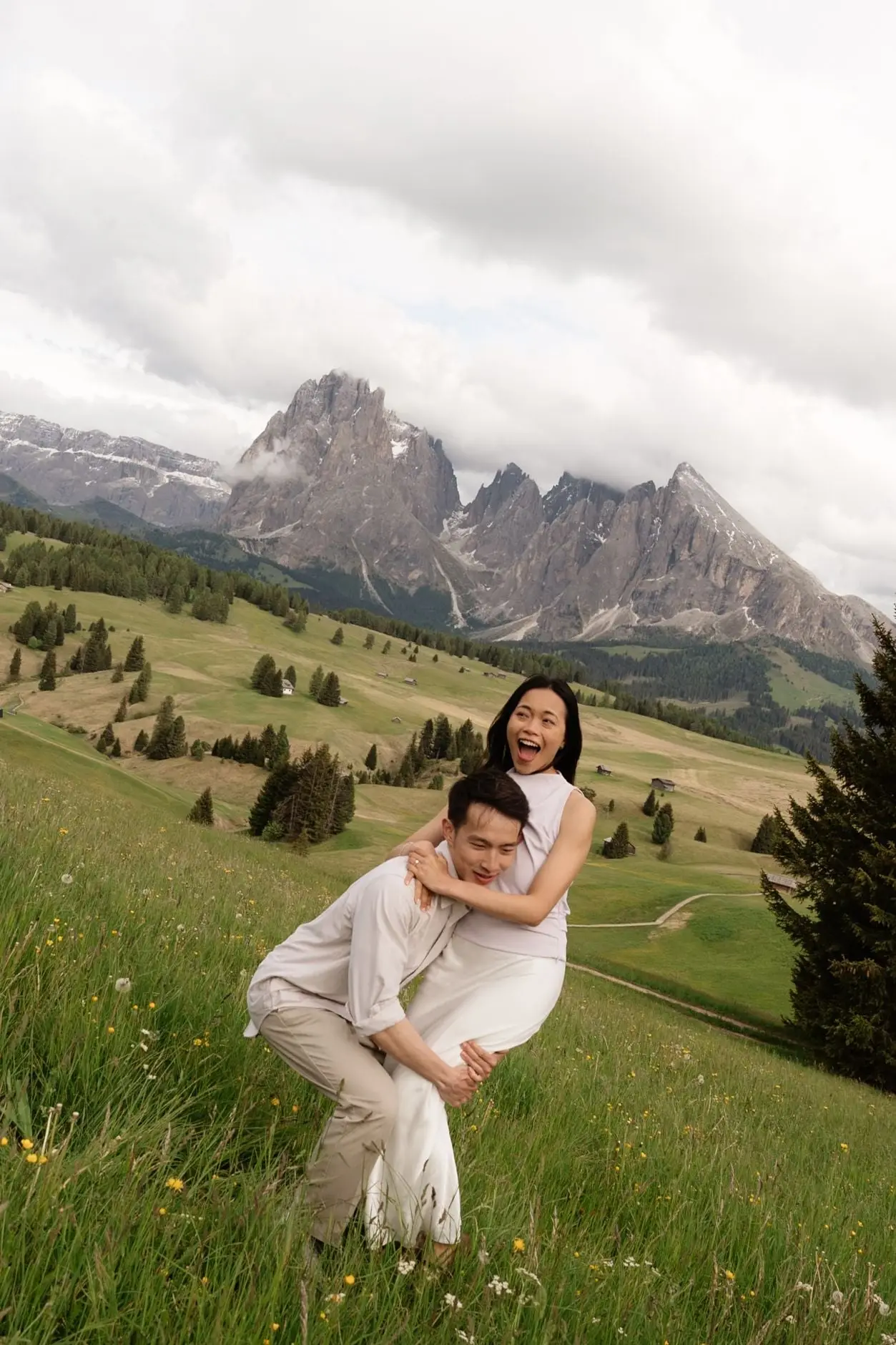 He lifts her piggyback style and she laughs, Dolomites peaks behind
