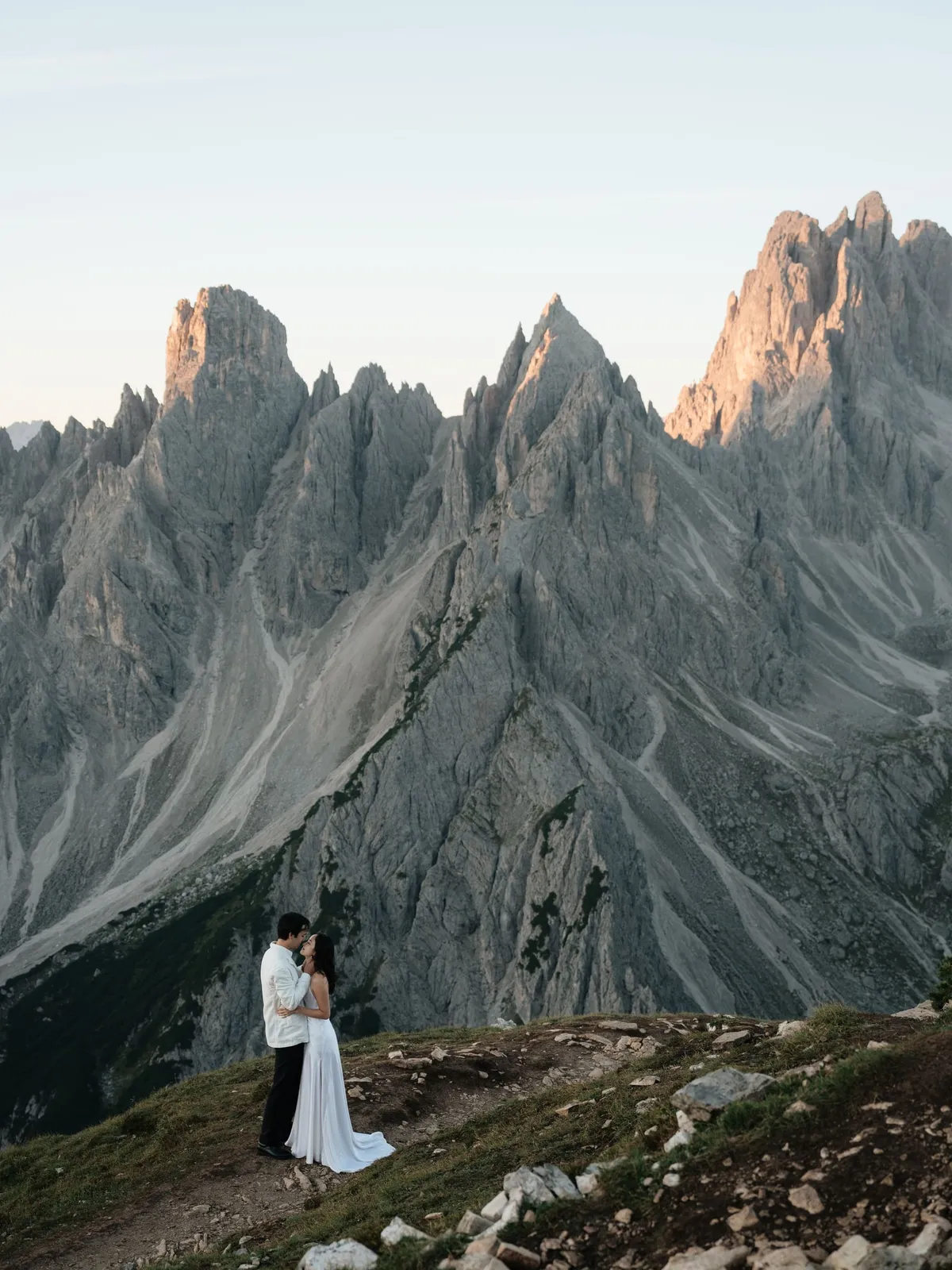 Couple embracing on a rocky ridge below the jagged Cadini di Misurina at first light