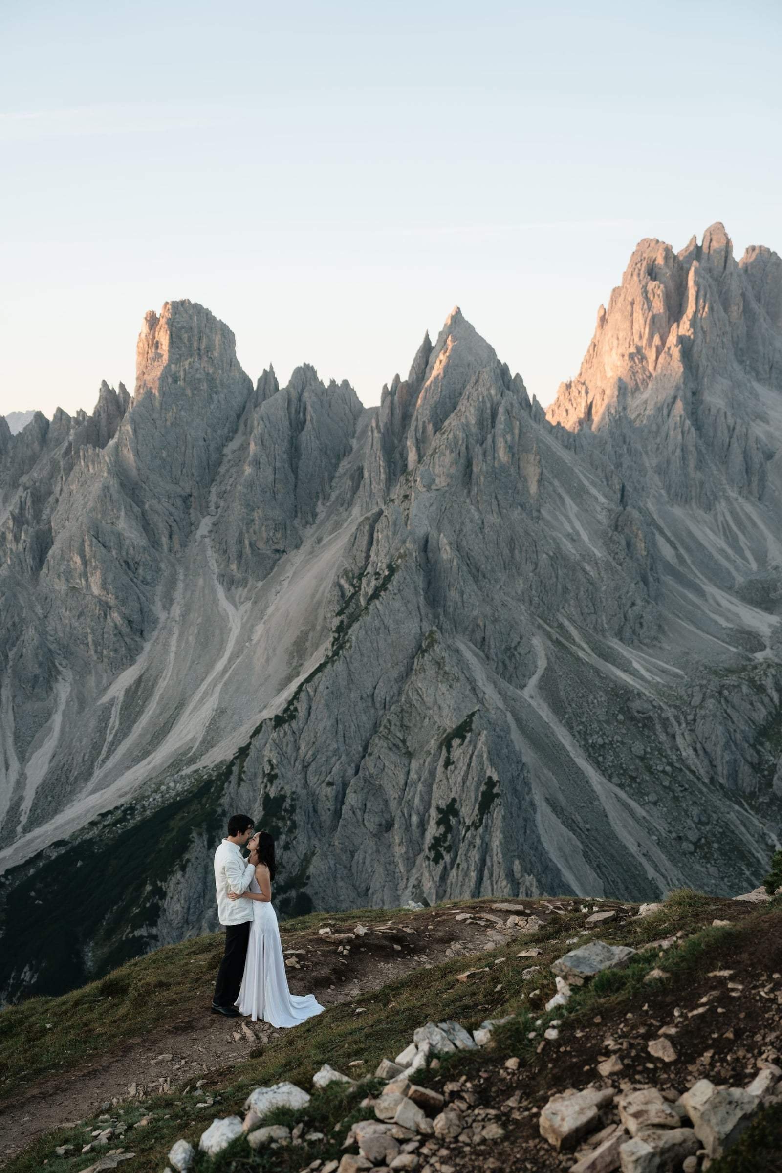 Couple embracing on a rocky ridge below the jagged Cadini di Misurina at first light