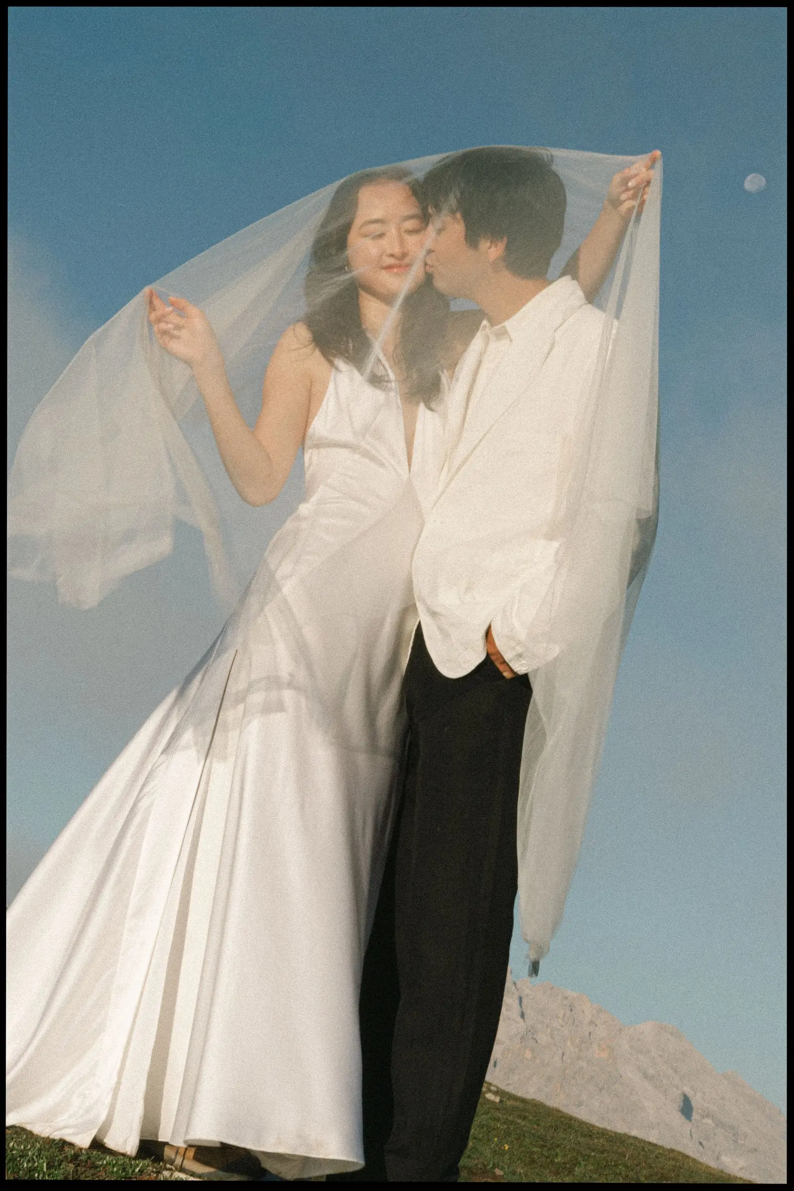 Couple kissing under a veil blowing in the wind, on film