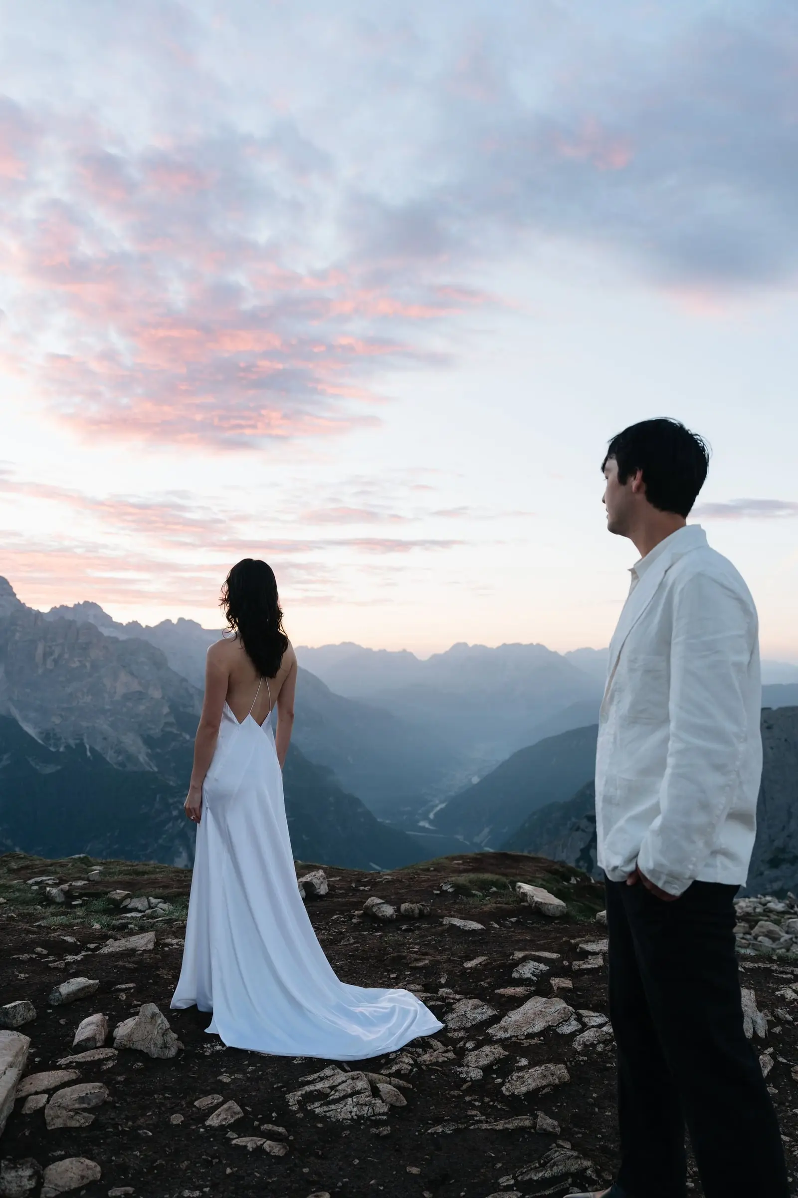 Bride in a backless gown looks over the valleys as the sky turns pink
