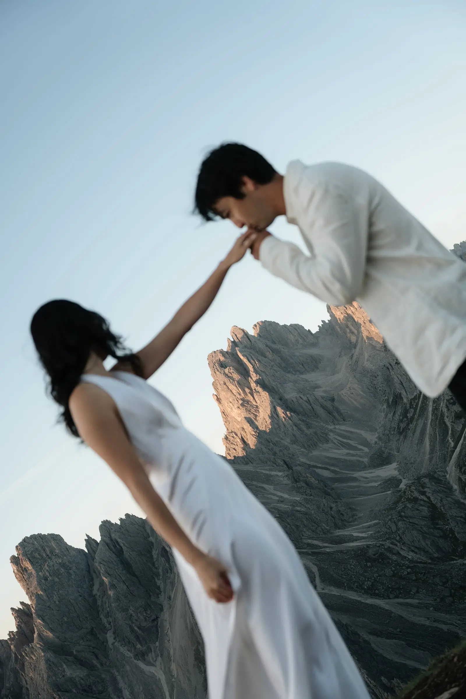 Groom kisses the bride's hand at the edge of the rocky ridge