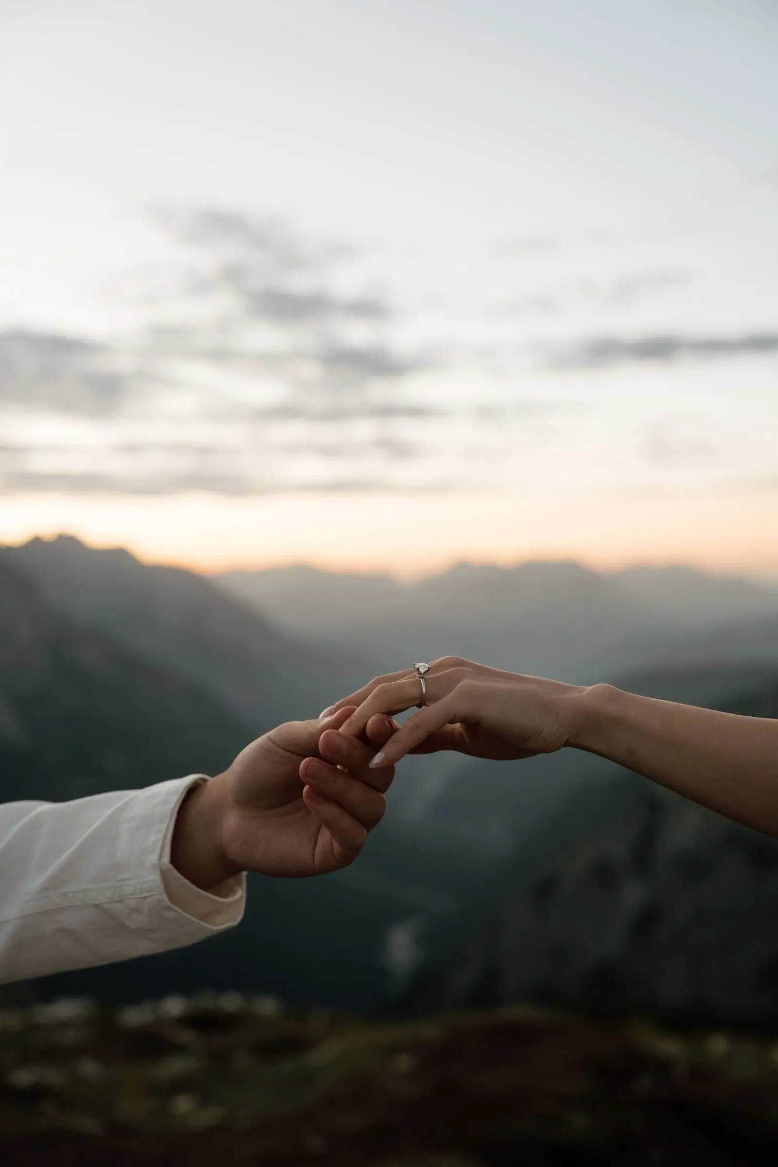 Two hands with rings reaching for each other against a hazy sunrise