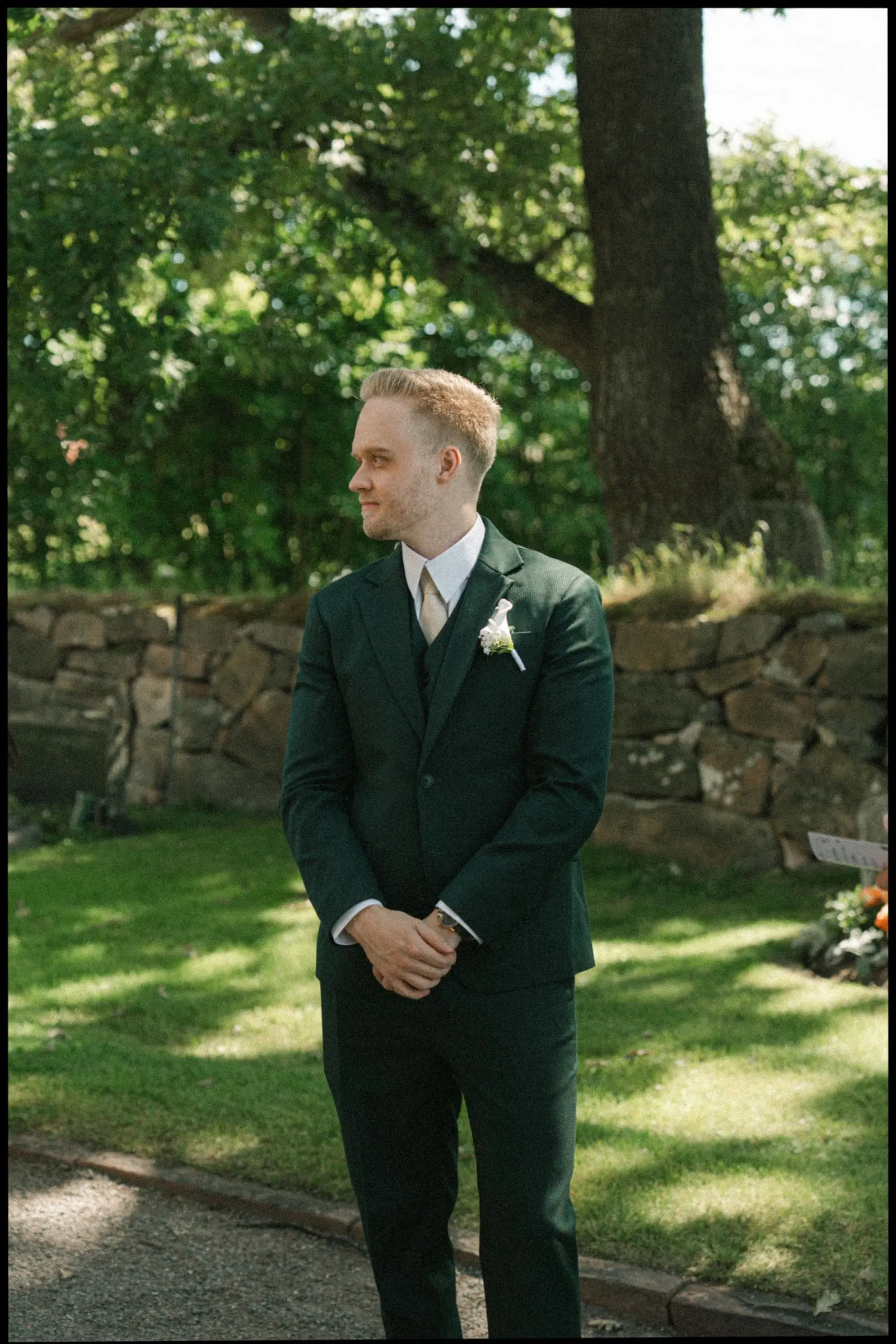 Groom in a dark green suit waiting in the churchyard, on film