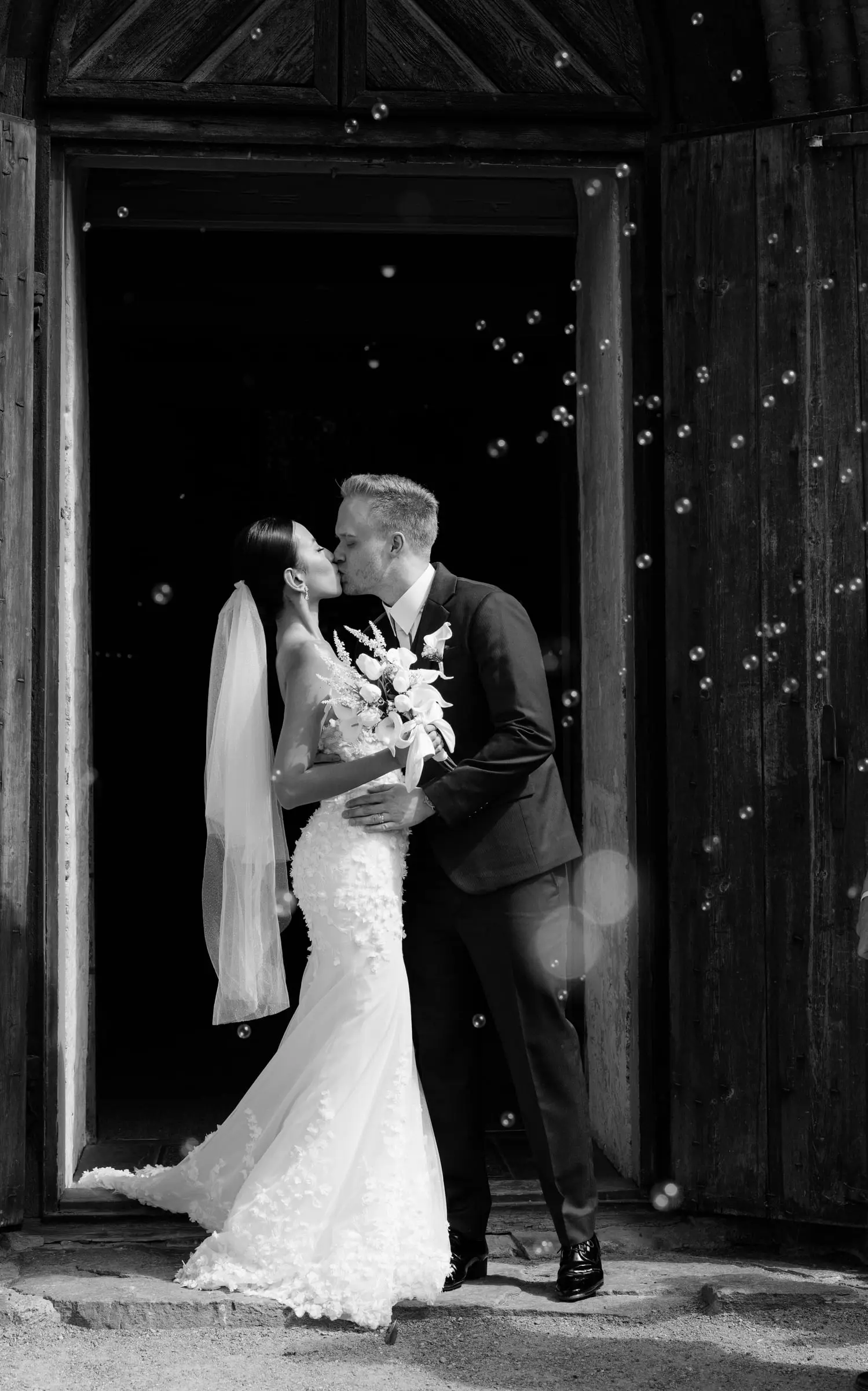 Black and white photo of the couple kissing in the church door among soap bubbles