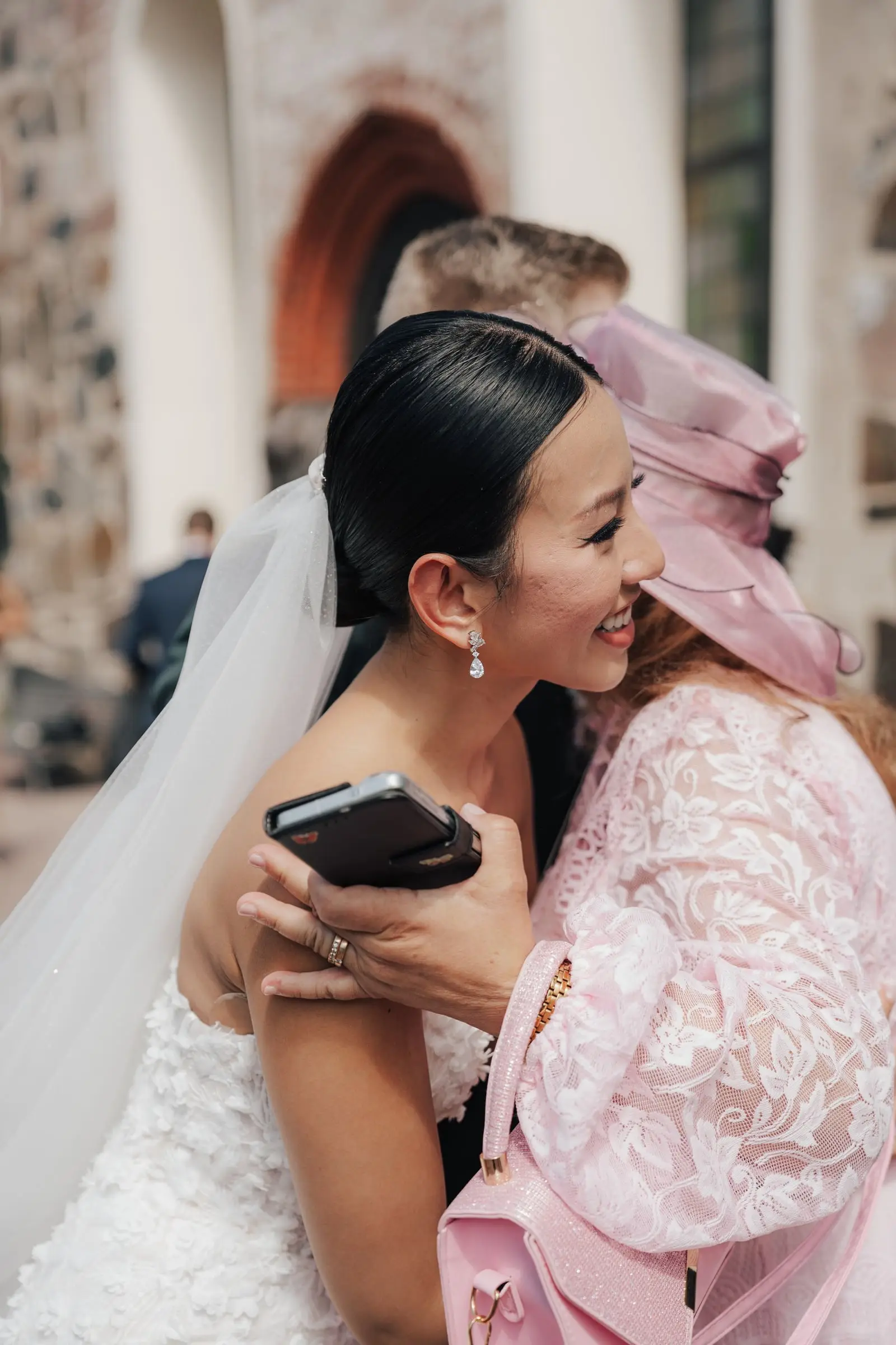 Bride hugging a guest in a pink hat outside the church