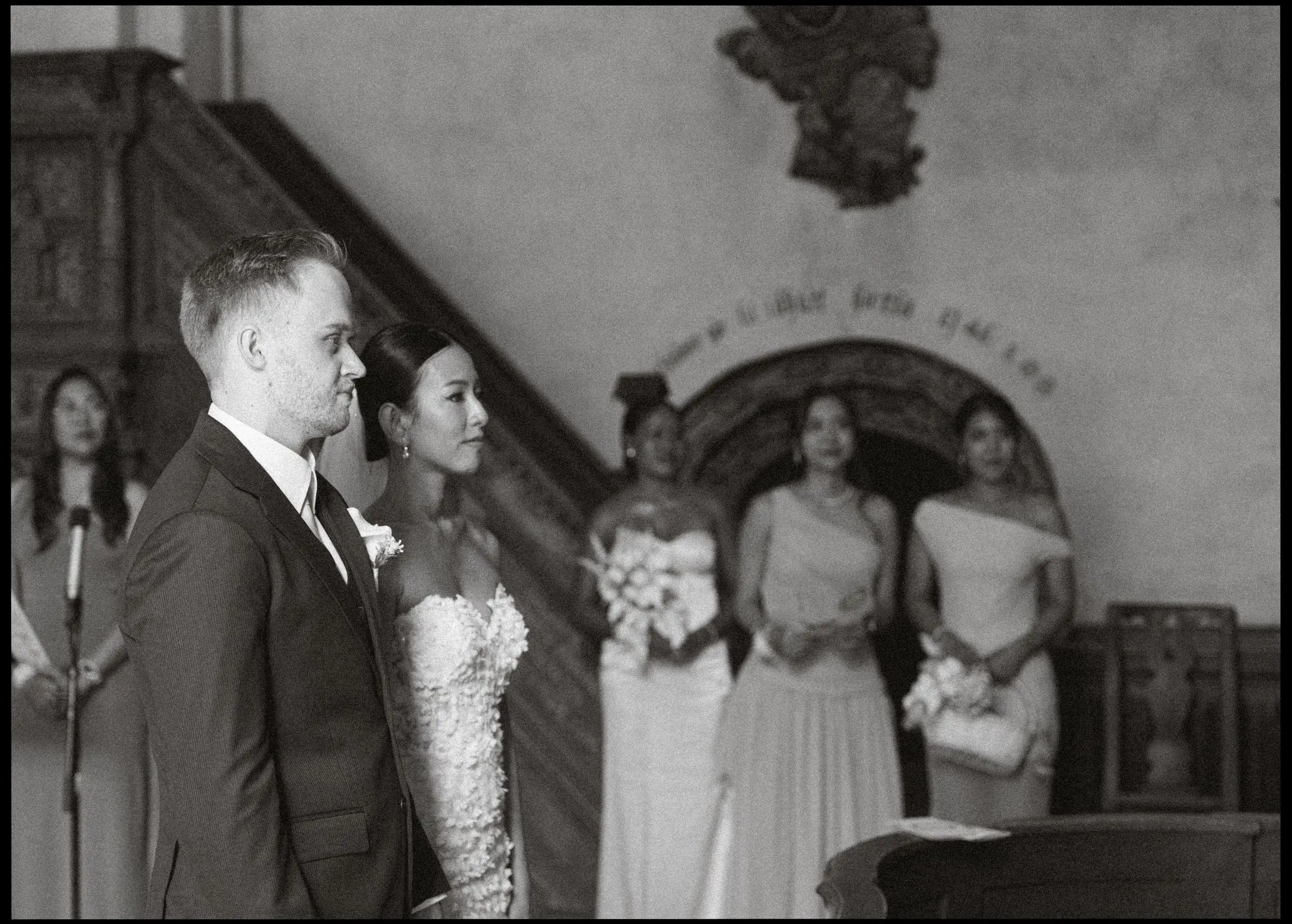 Black and white photo of the couple at the altar with the bridesmaids, on film