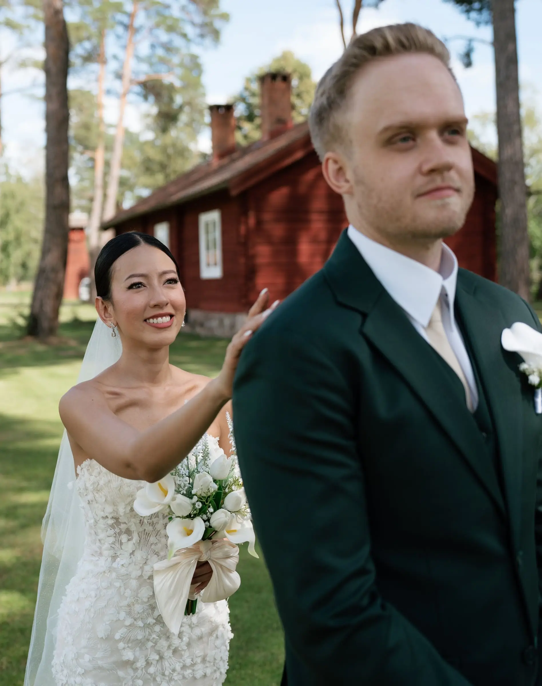 Bride touches the groom's shoulder for the first look in front of a red house