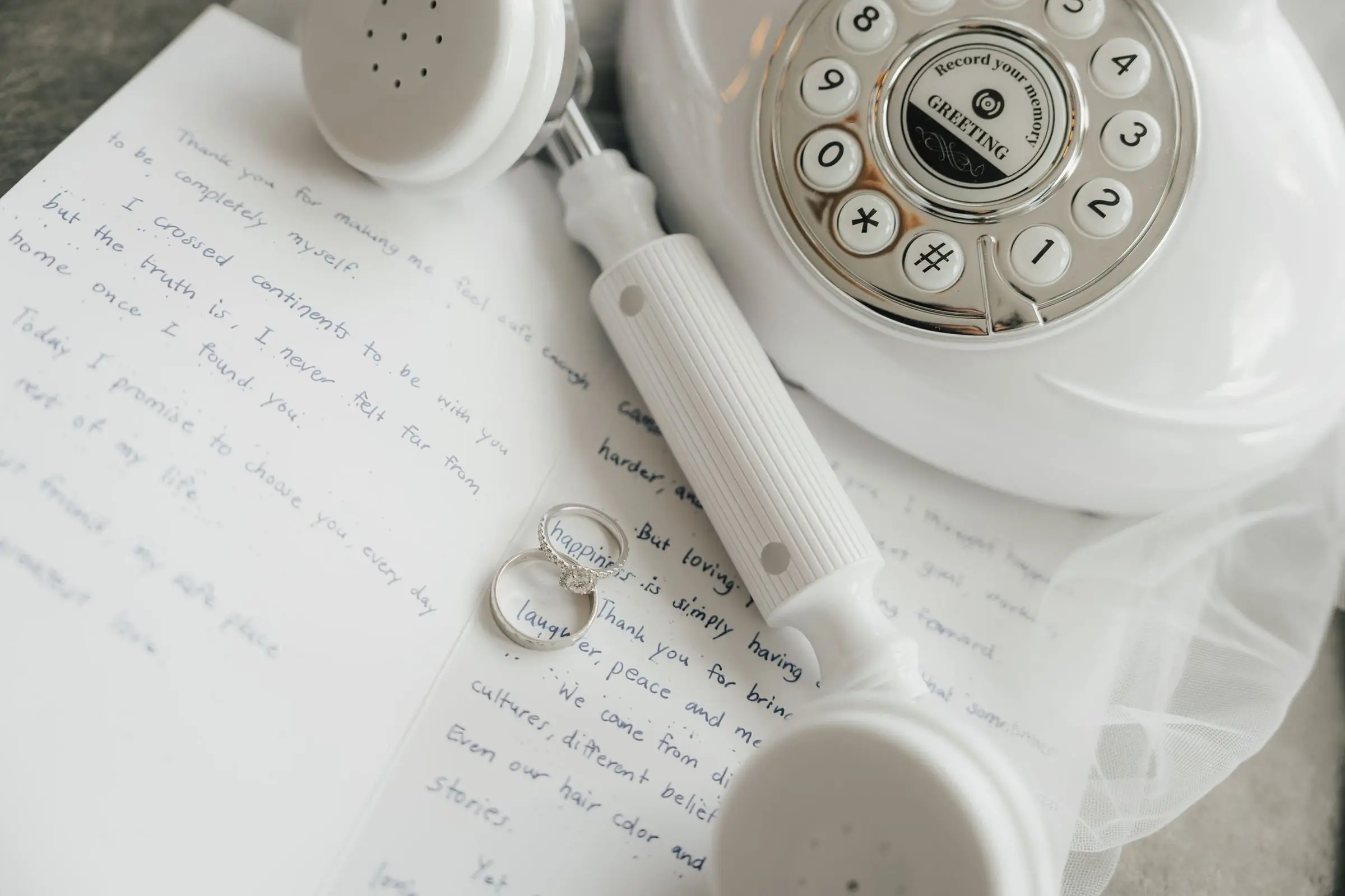 Wedding rings, handwritten vows and a white vintage telephone