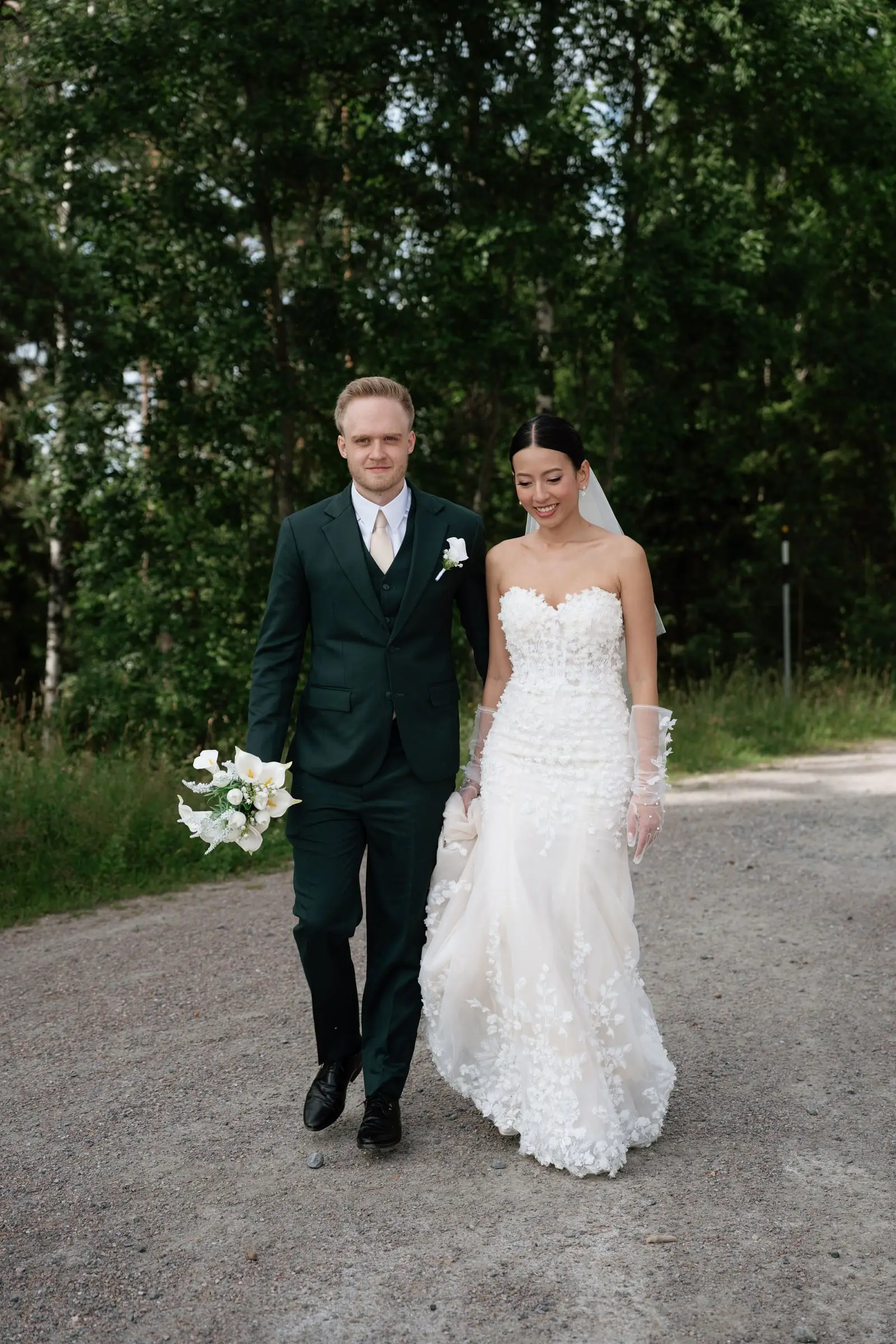 Newlyweds walking hand in hand along a gravel road through the forest