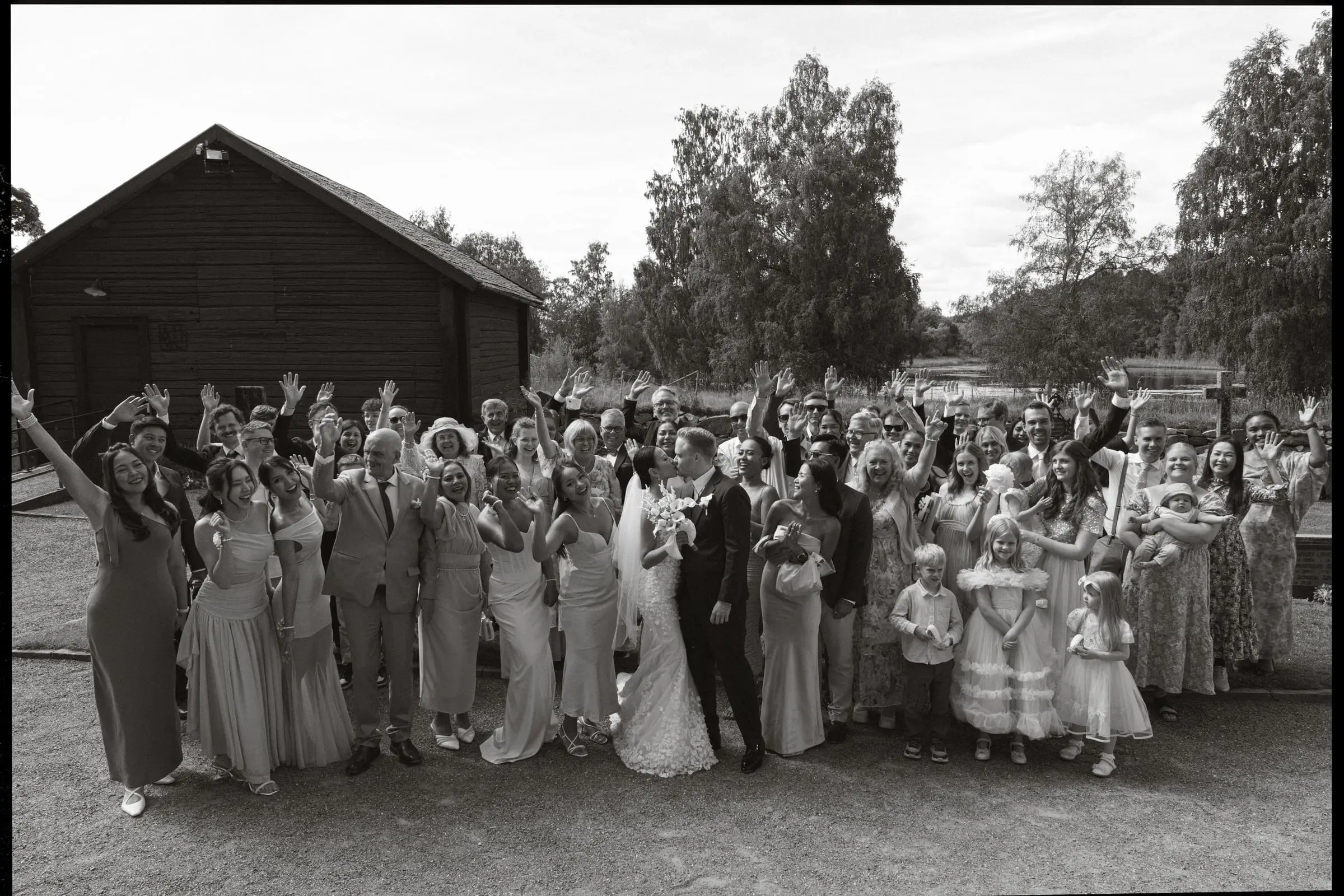 Black and white group photo of all the guests cheering by a wooden house