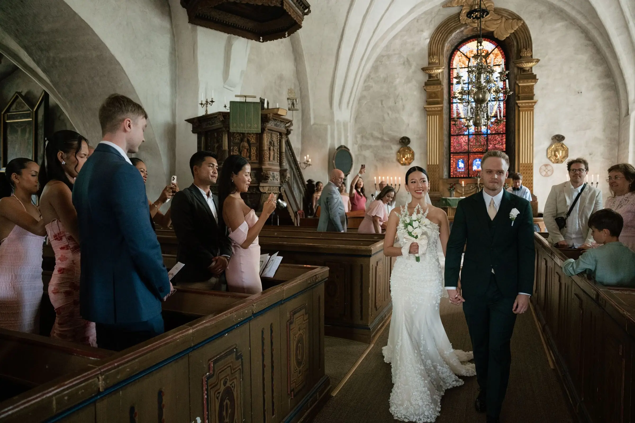 Groom and bride walking down the aisle of the church as guests stand