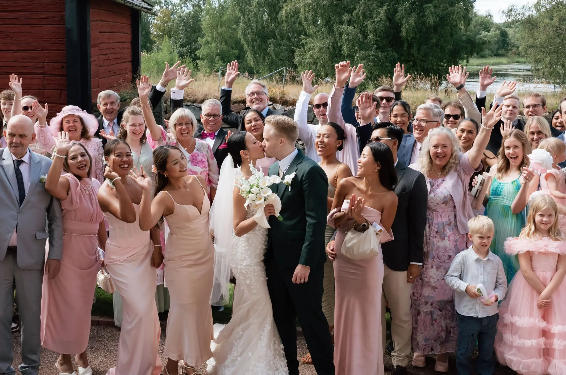 Group photo of the cheering guests with the couple kissing in the middle