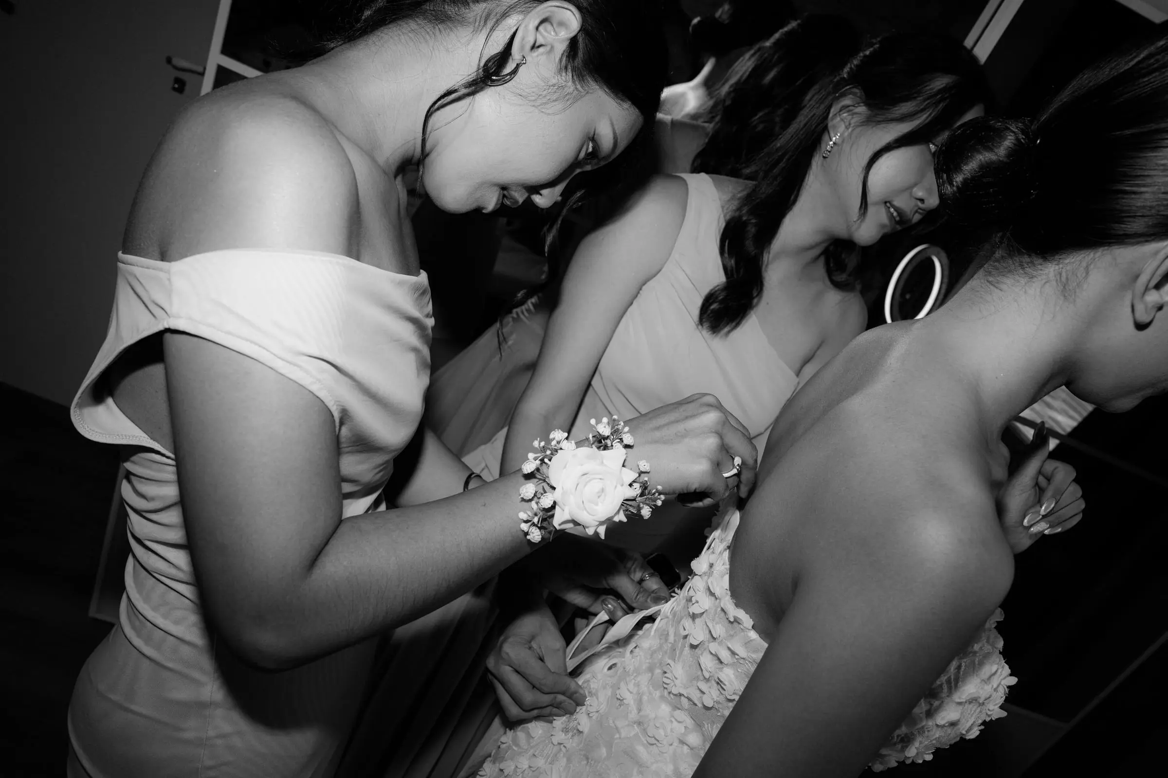Black and white photo of bridesmaids helping the bride with her dress