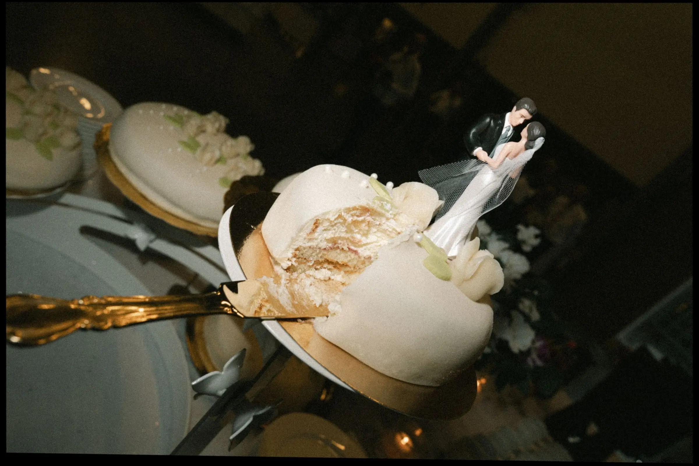 Wedding cake with a bride and groom topper and a gold cake knife, on film