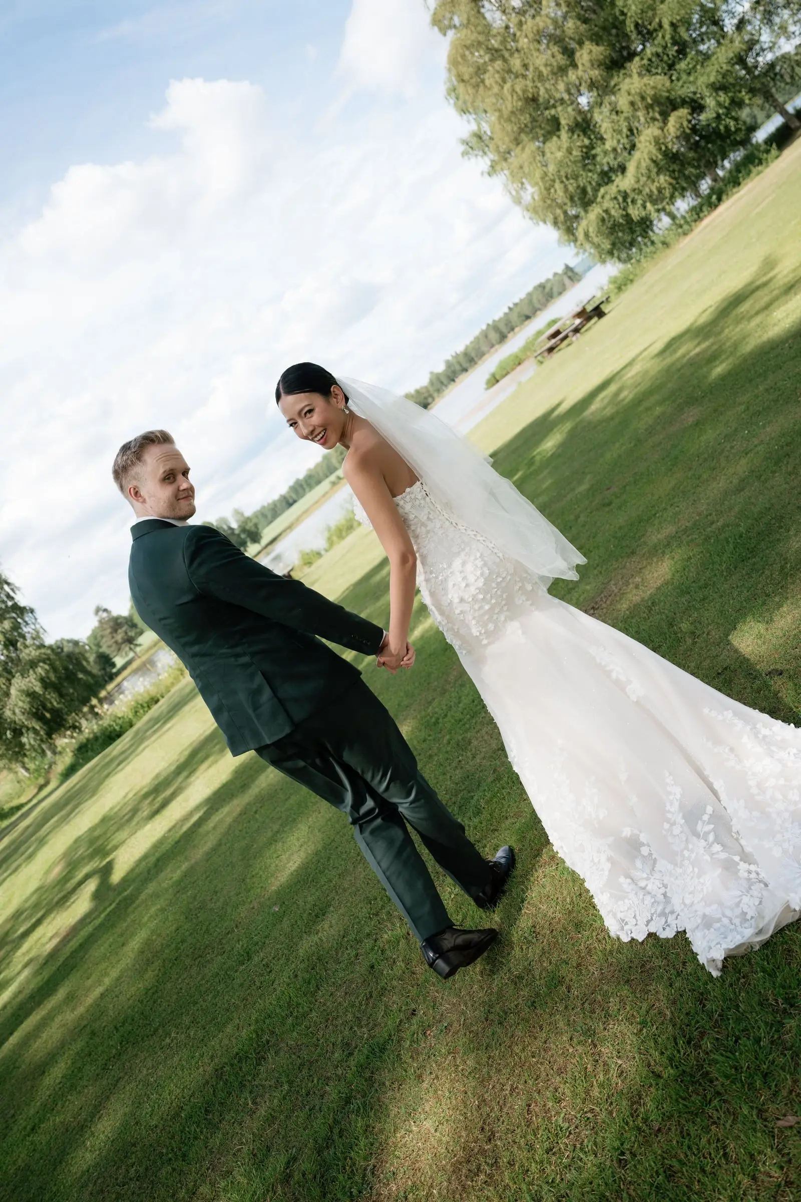 Newlyweds walking hand in hand on the lawn by a lake