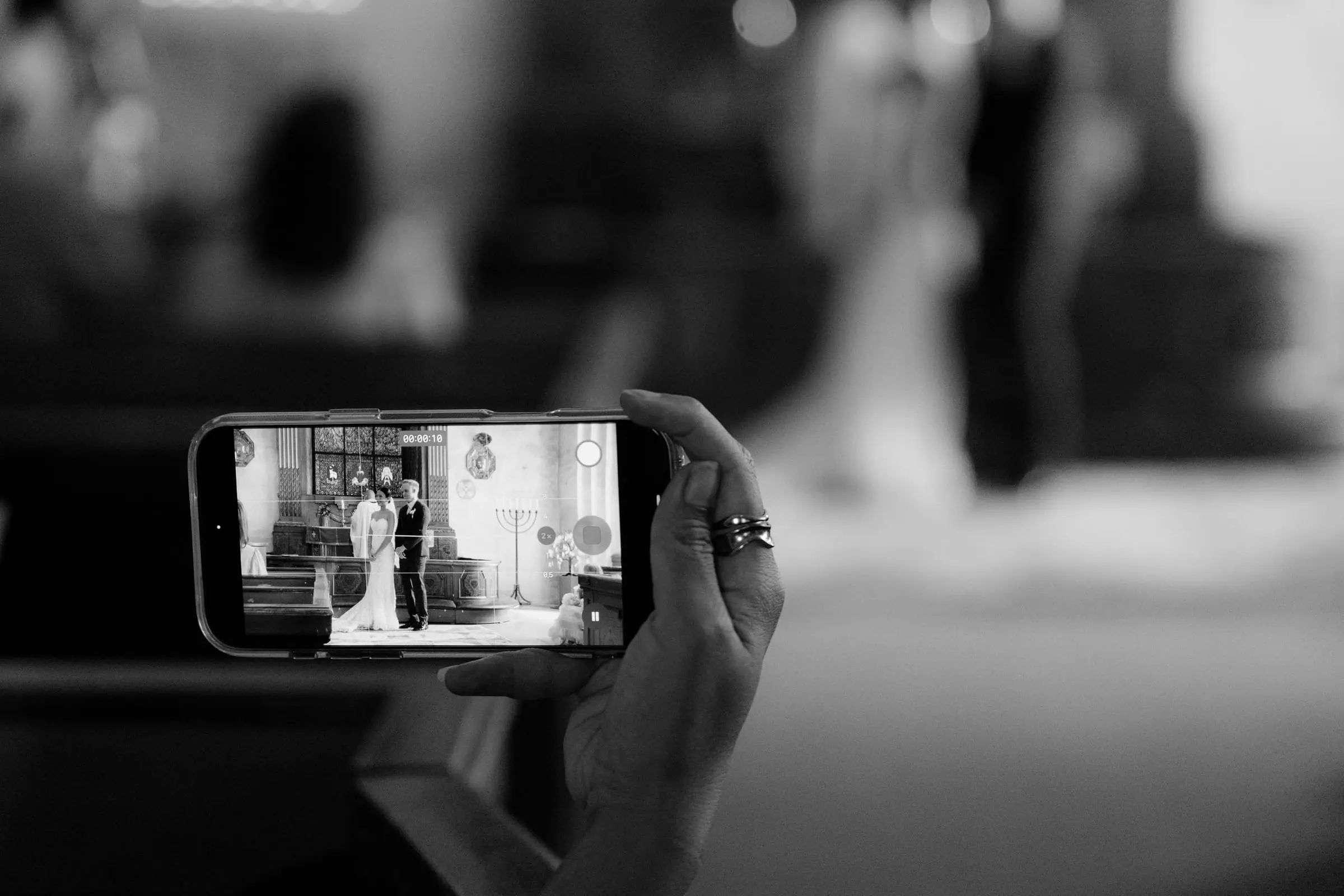 Black and white detail of a guest filming the ceremony on a phone