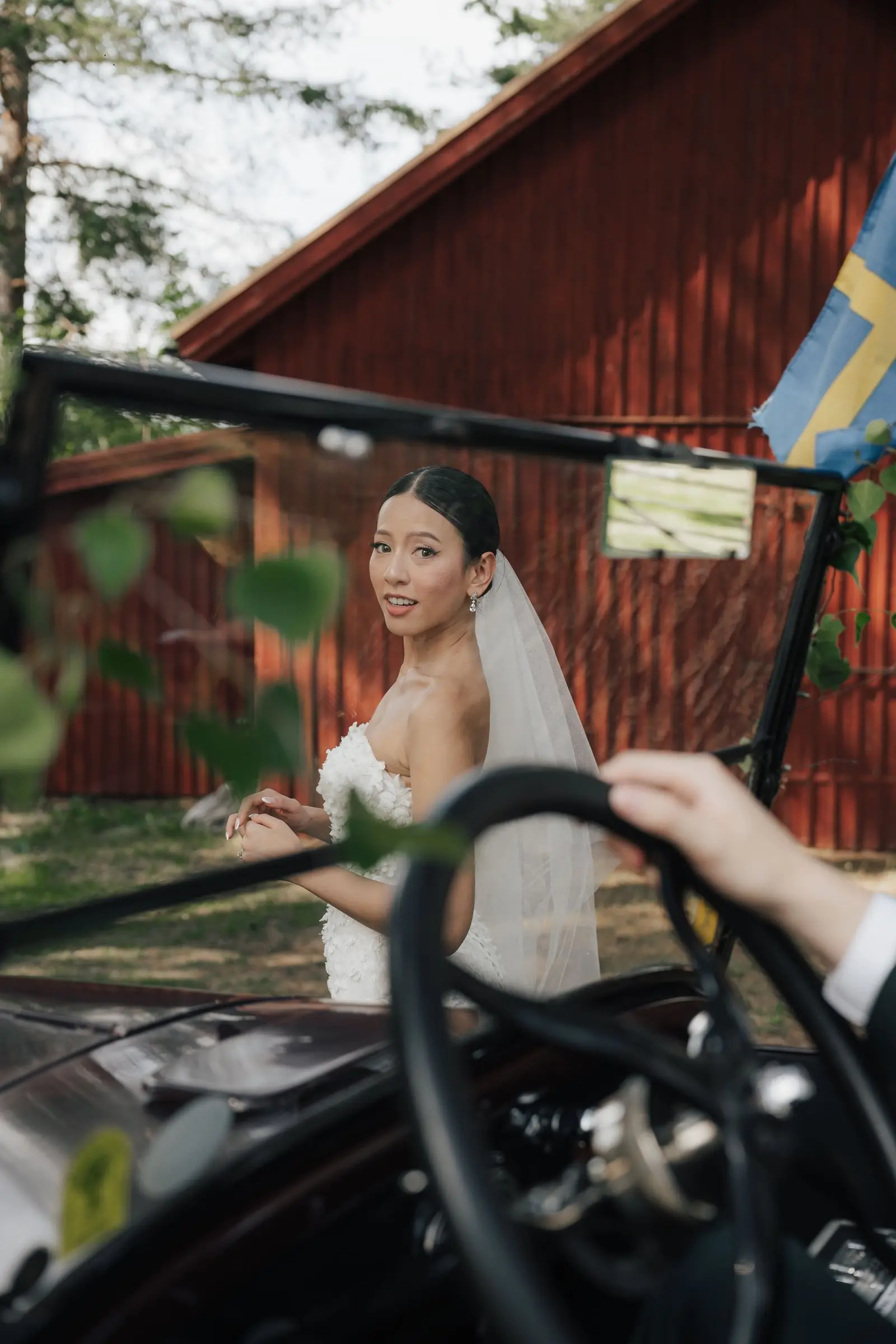 Bride seen through the windscreen of the vintage car by a red house