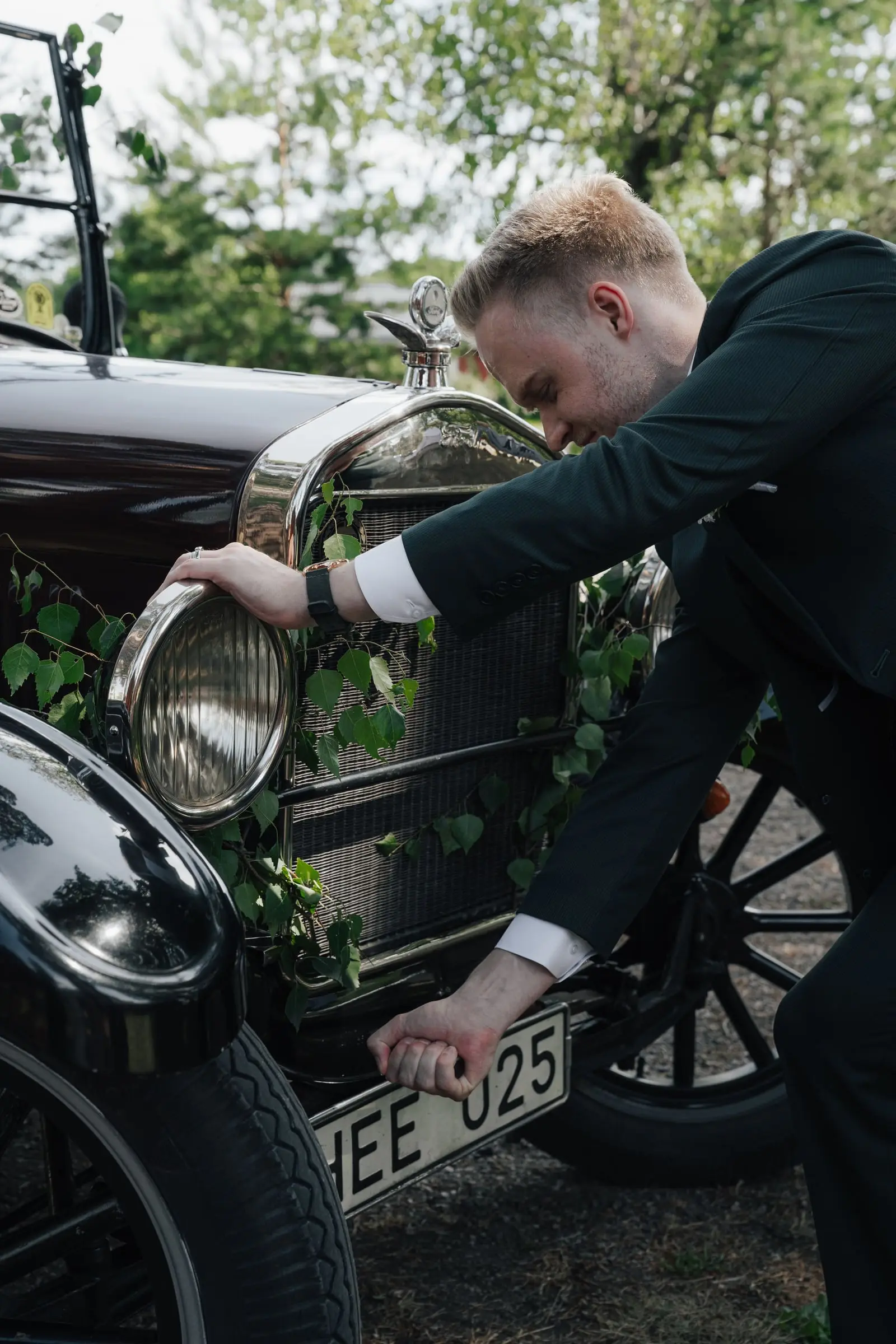 Groom checking the vintage car decorated with greenery