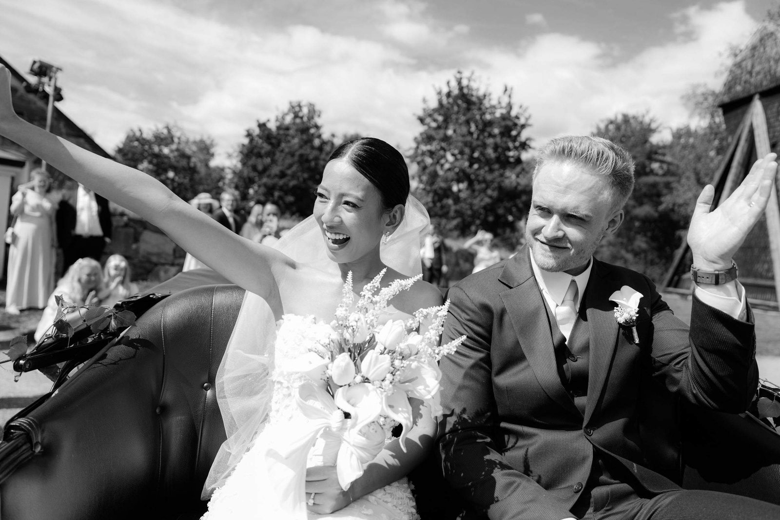 Black and white photo of the bride waving from the car