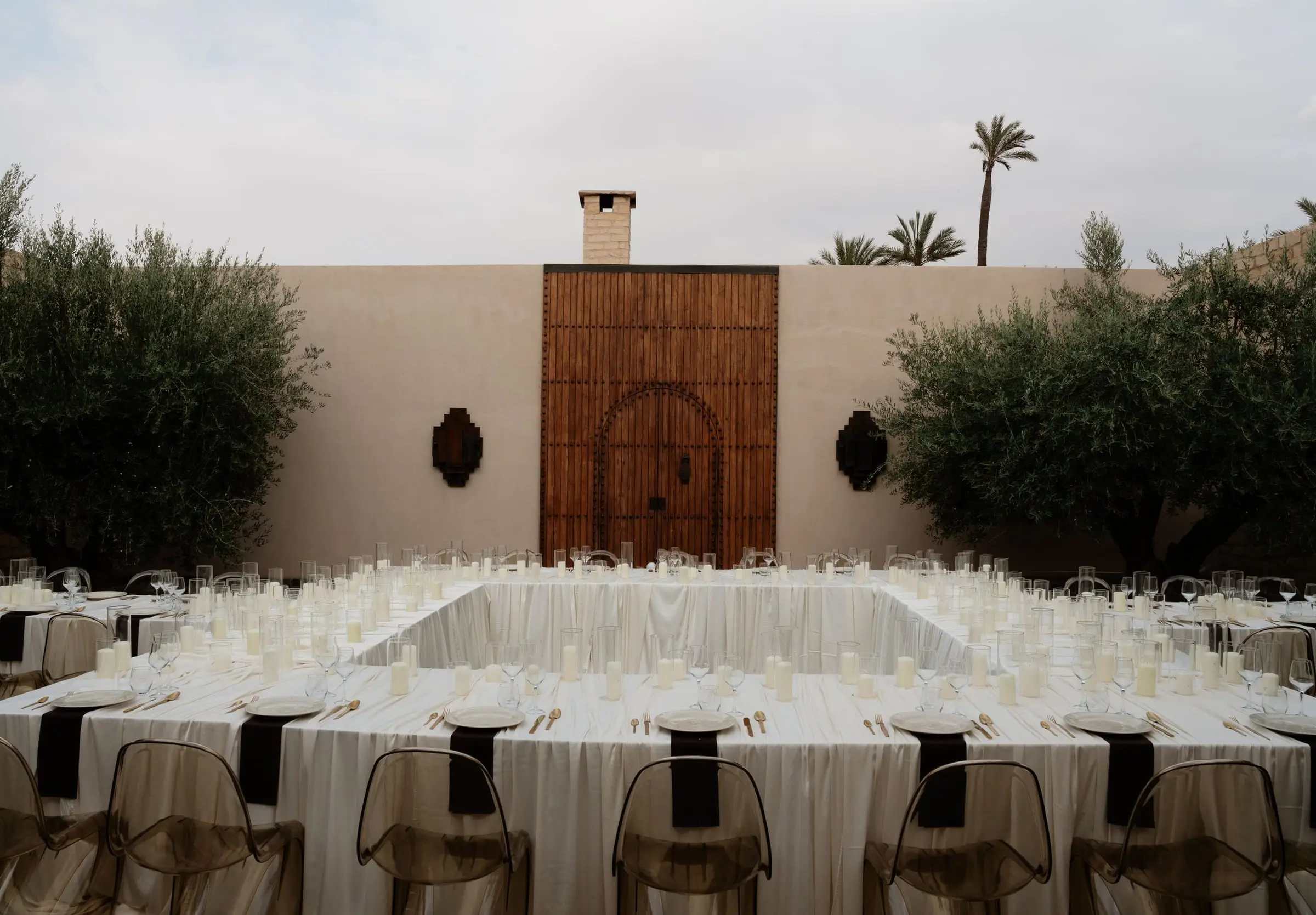 Square dinner table set in a courtyard with a carved wooden door and palm trees