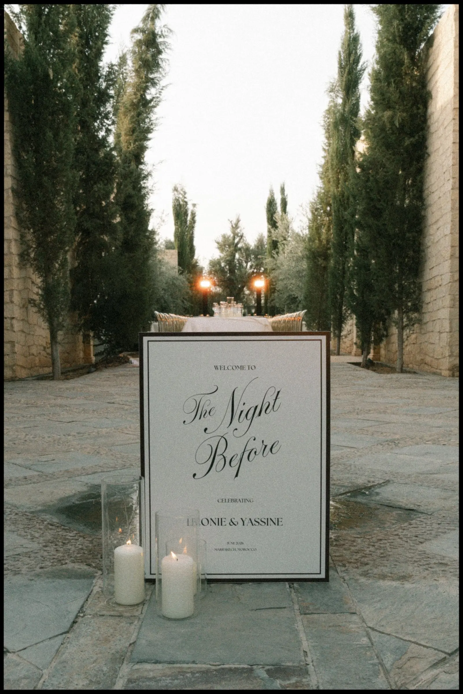 Welcome sign reading The Night Before between candles and cypresses, on film