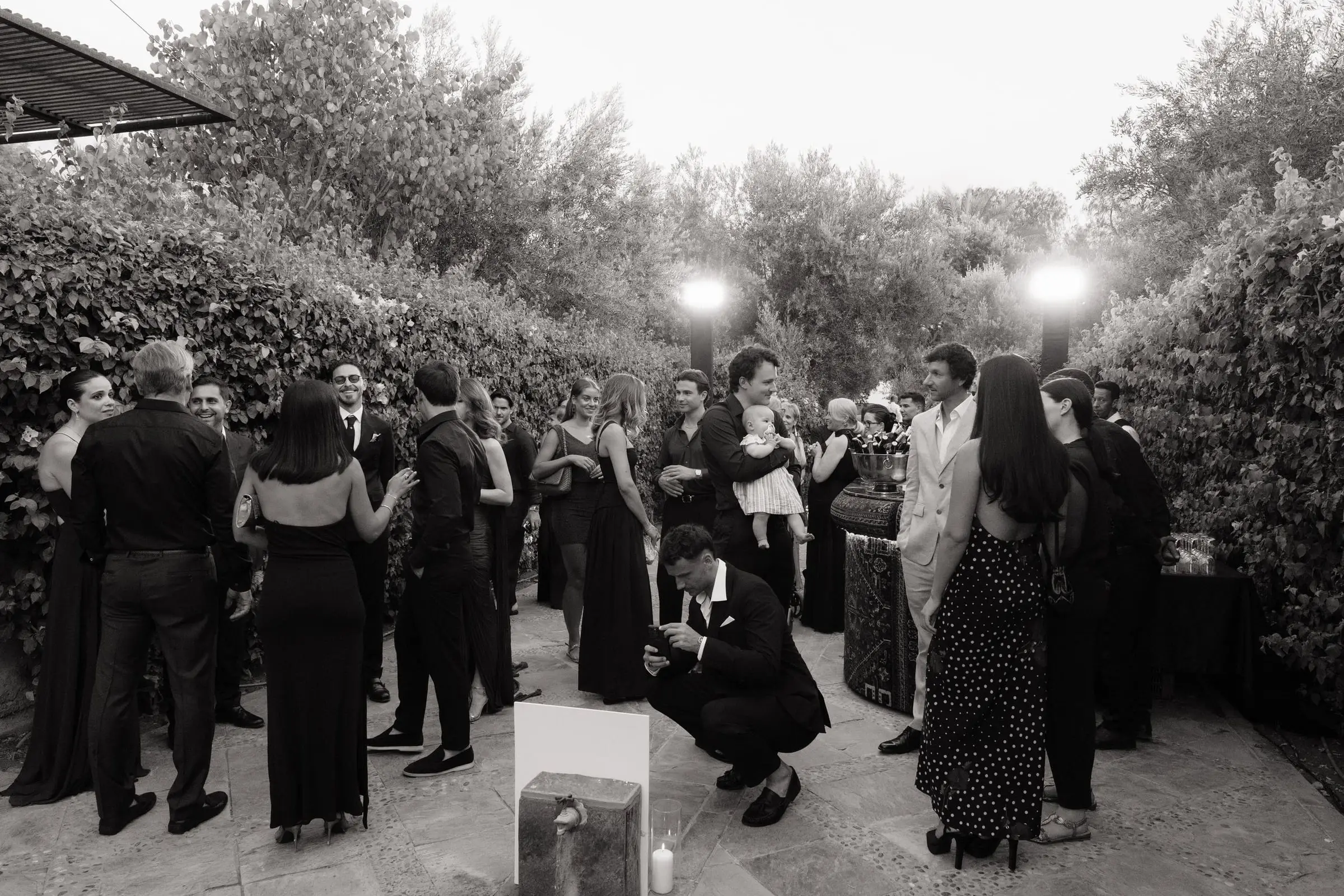 Black and white photo of guests gathering in the garden at dusk