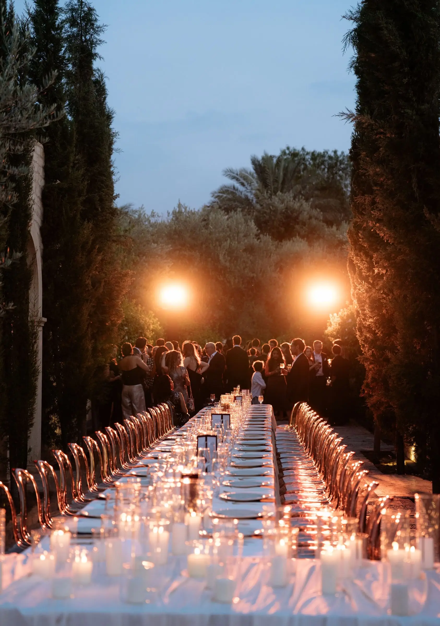 Candlelit dinner table stretching between cypress trees at dusk