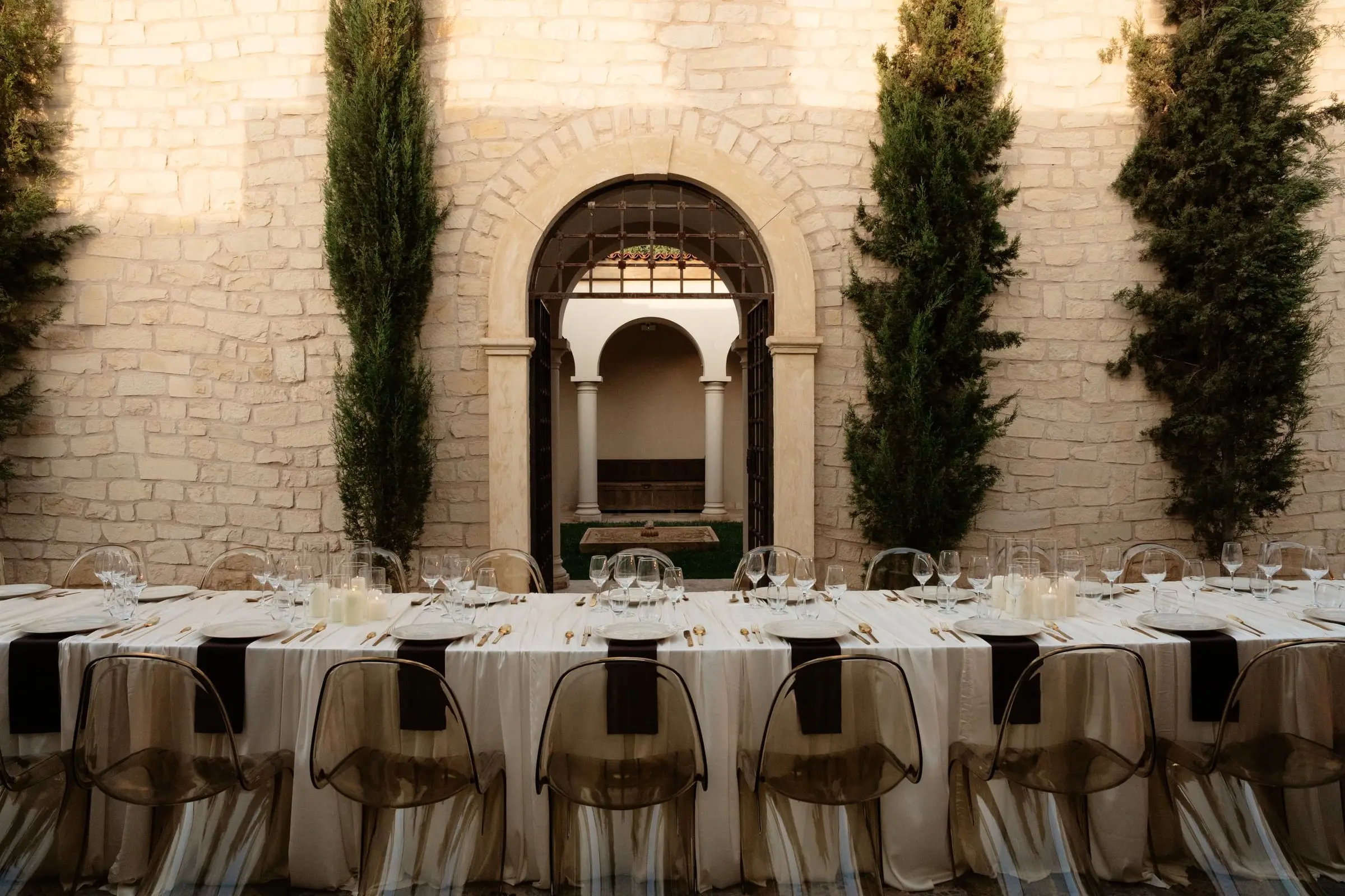 Long dinner table set in front of the arched palace wall and cypresses