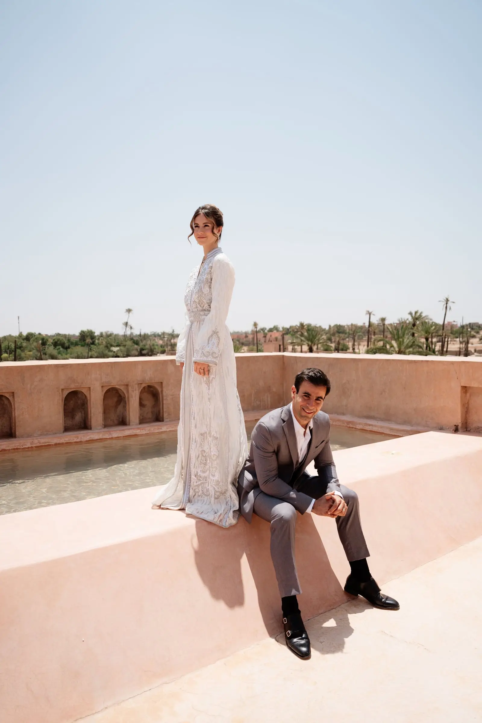 Bride in a white kaftan and groom on a rooftop terrace overlooking the palm grove