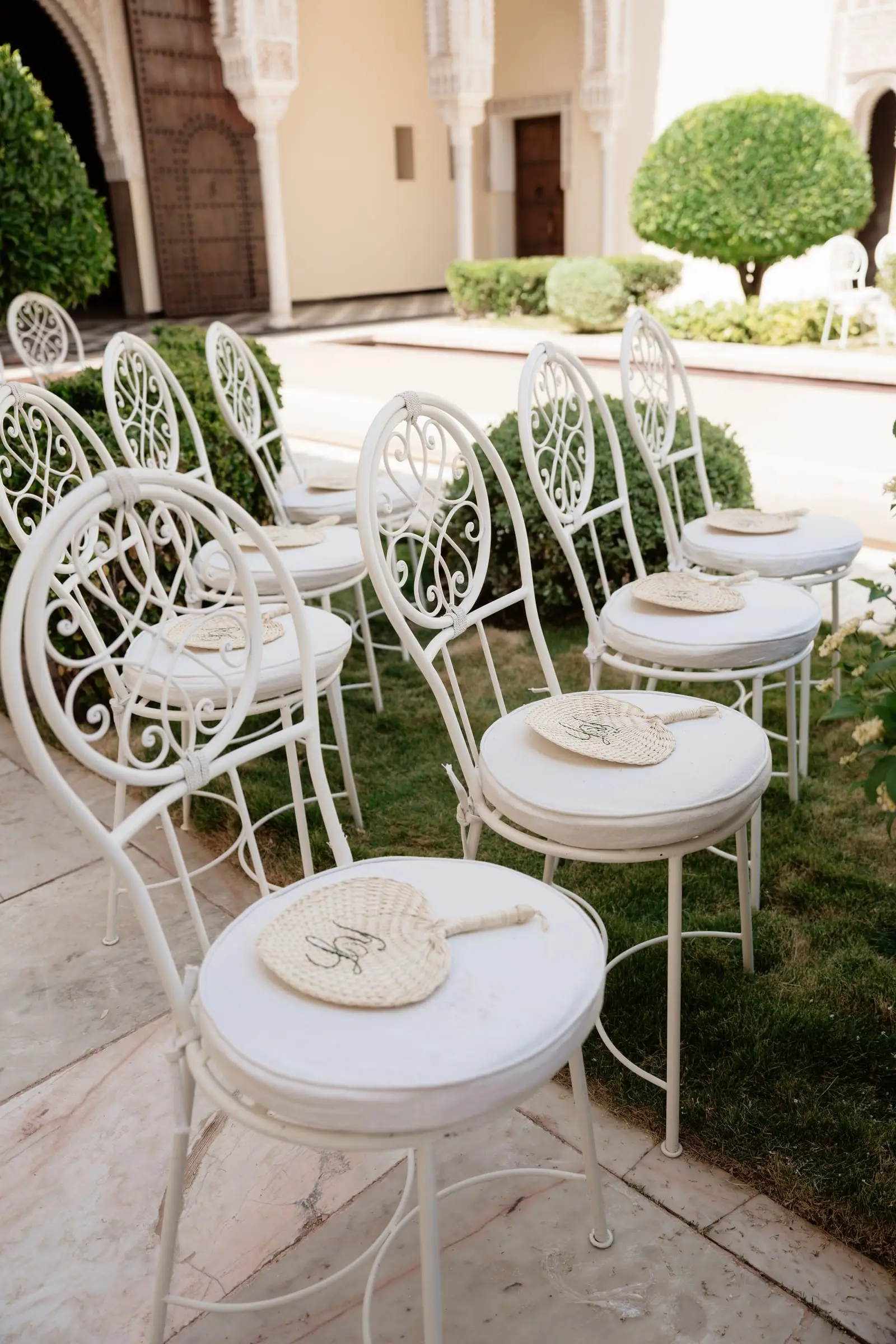 White wrought-iron ceremony chairs with fans in the palace garden